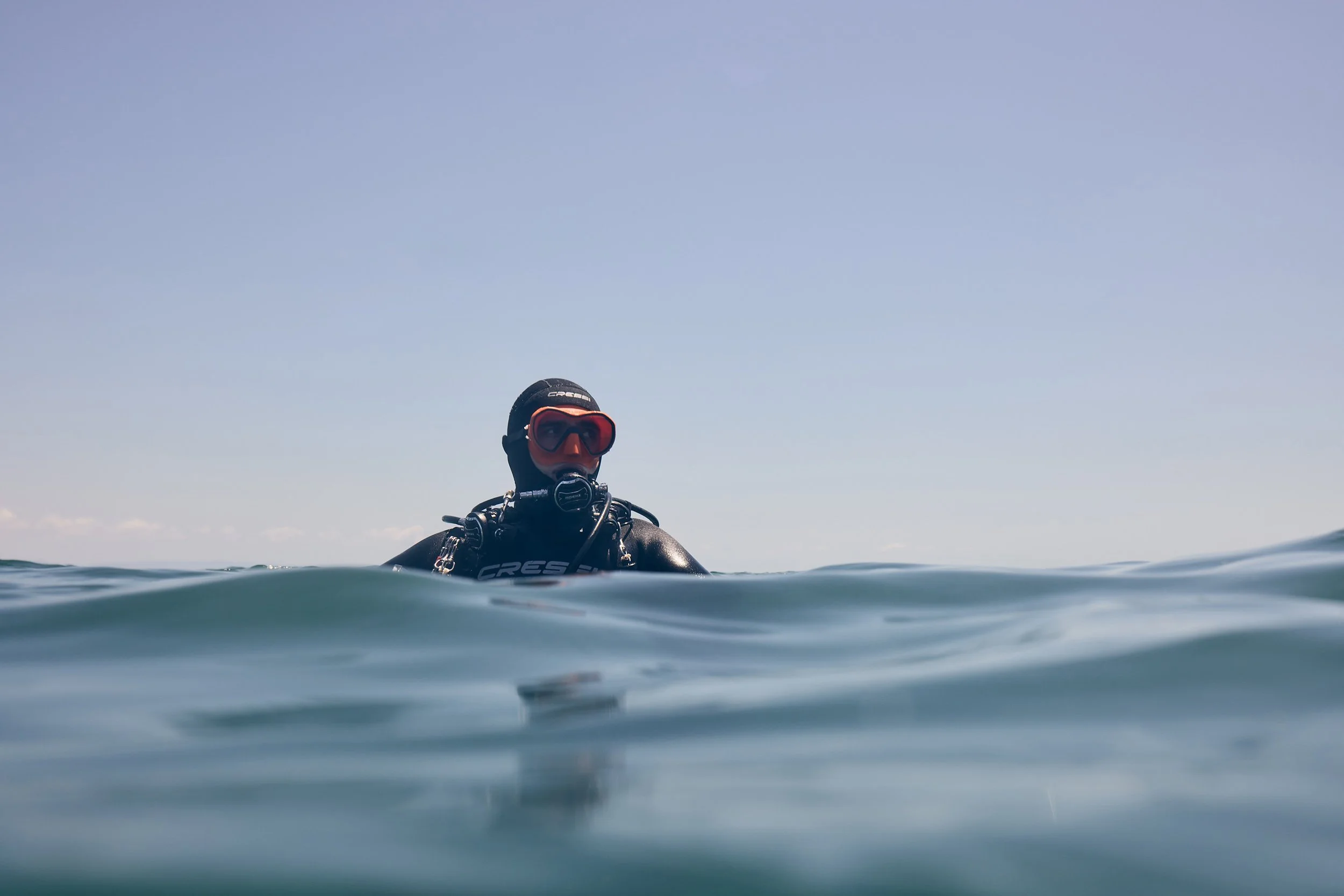 A person in a wetsuit and diving mask partially submerged in the ocean, with the sky visible above.