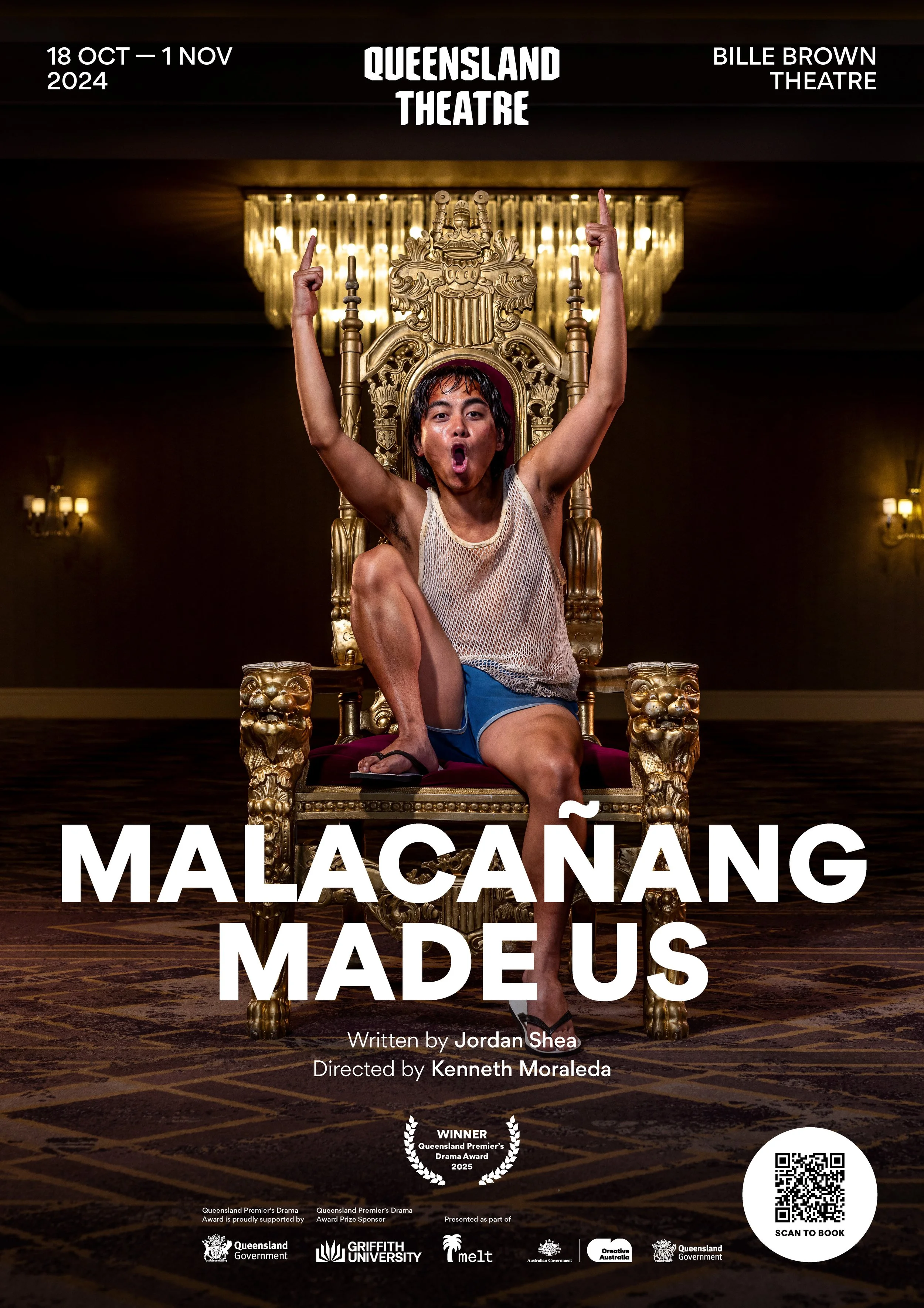 A person sitting on an ornate golden throne, one leg crossed over the other, raising both arms with index fingers pointing upward, on a stage with a chandelier in the background. The person is wearing a mesh tank top and blue shorts. The top of the p