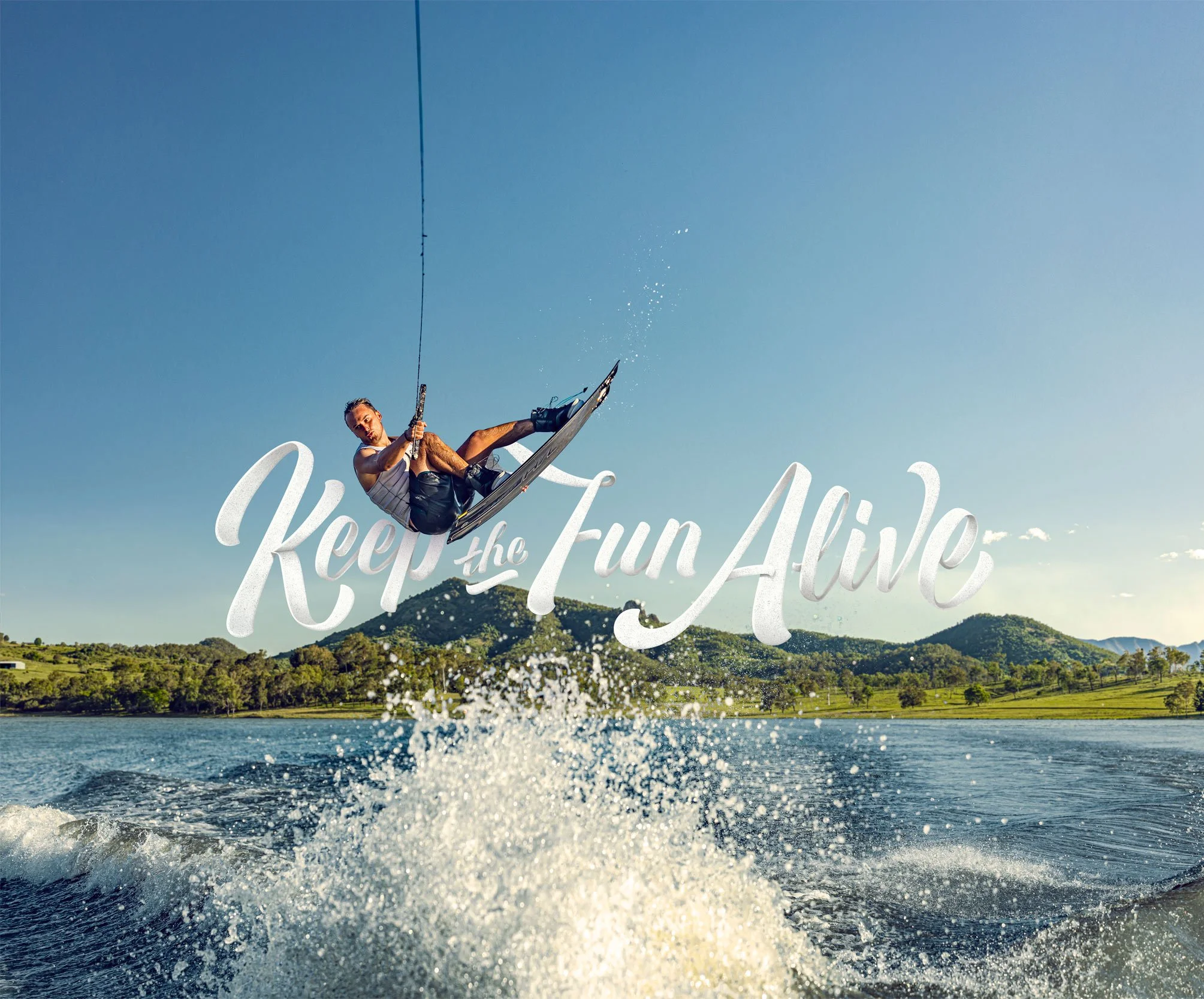 Person wakeboarding on a lake with a mountain in the background and blue sky overhead.