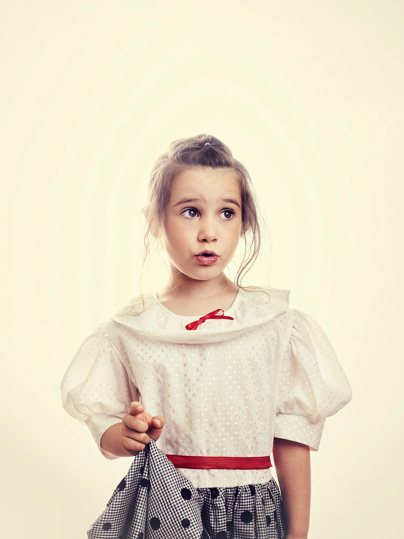A young girl with a surprised expression, wearing a white polka-dot blouse with puffed sleeves, a red ribbon, and a black and white checkered skirt, holding a matching checkered cloth.