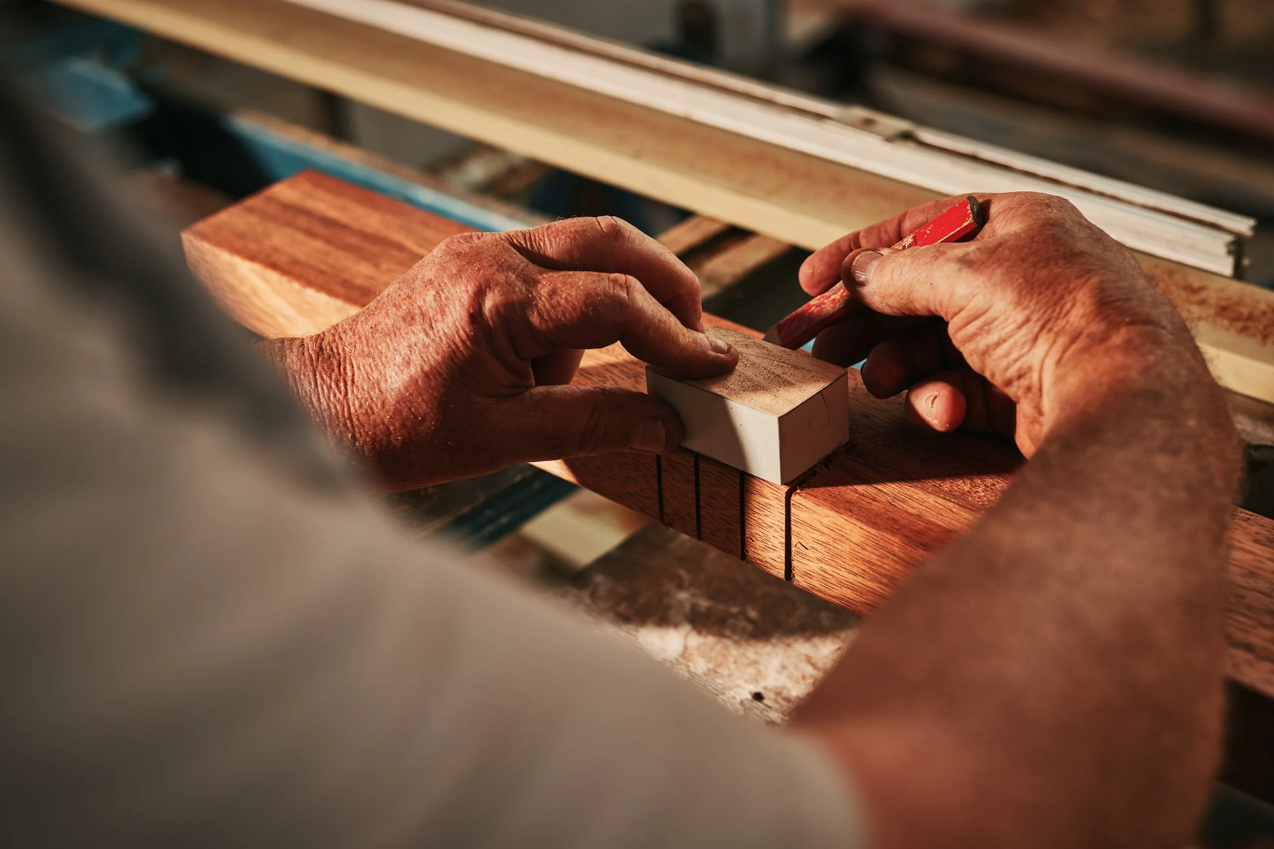 Close-up of hands working with woodworking tools on a piece of wood, in a woodworking shop.