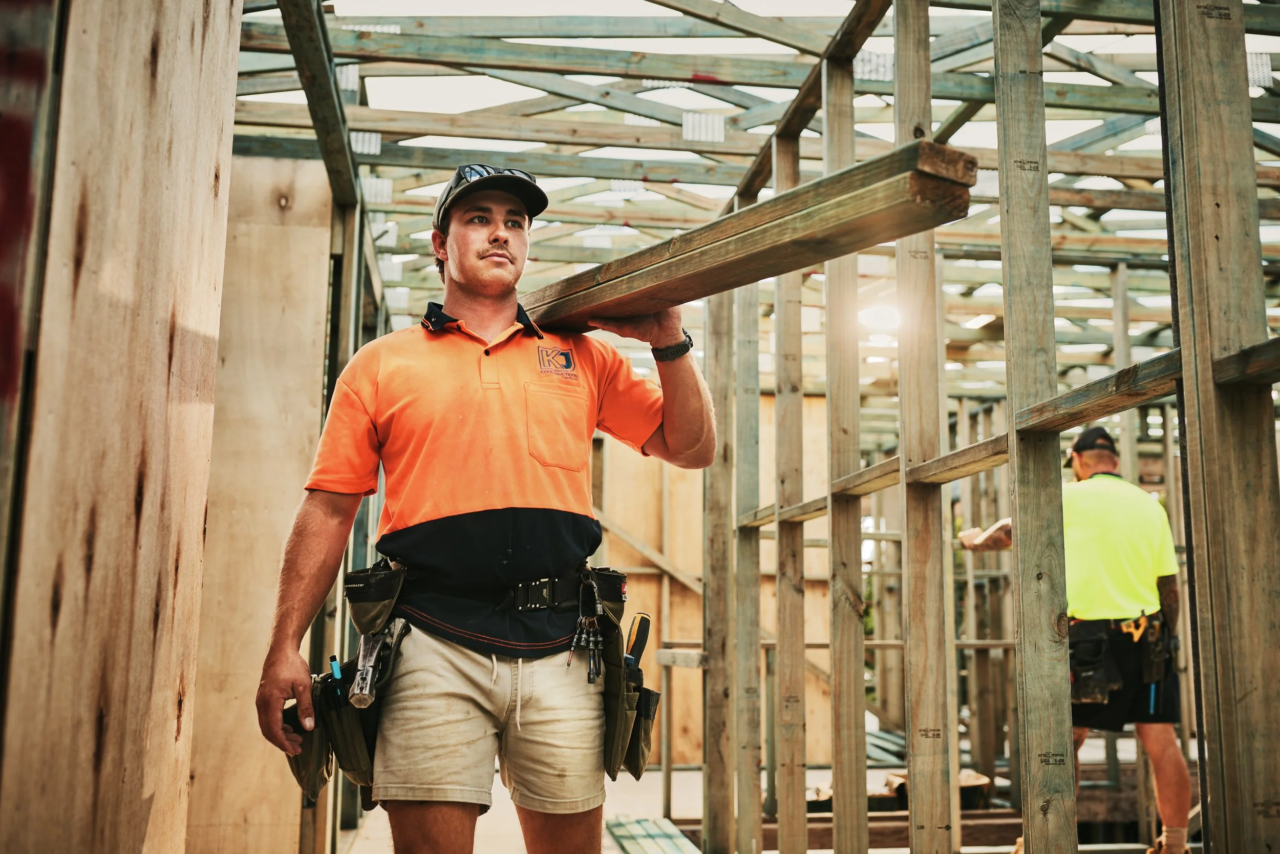 Construction worker carrying a wooden plank at a building site with wooden framing and scaffolding.