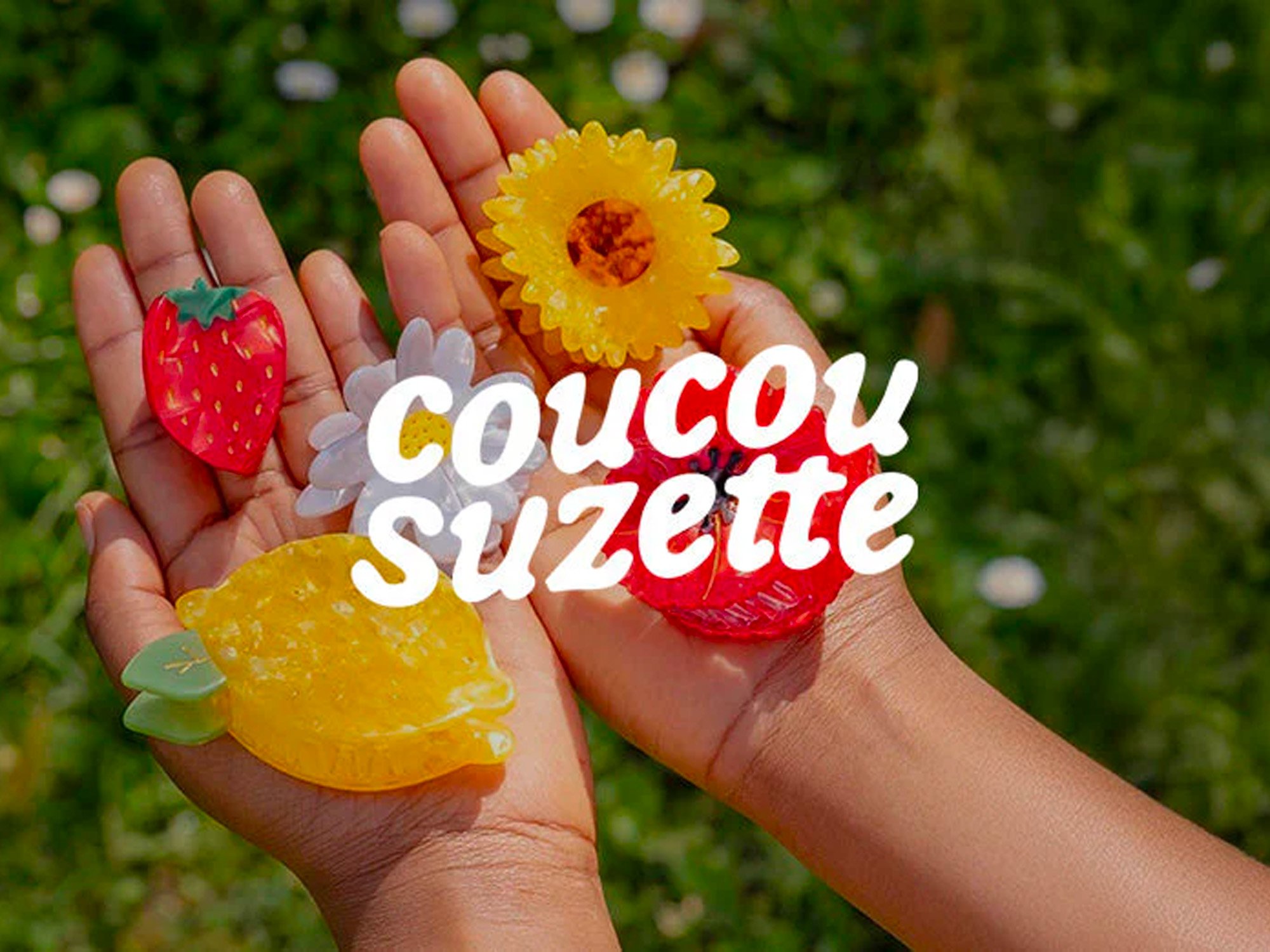 Mains d'enfants tenant des bonbons en forme de fraise, citron, marguerite, et tournesol, avec texte "coucou suzette" en blanc