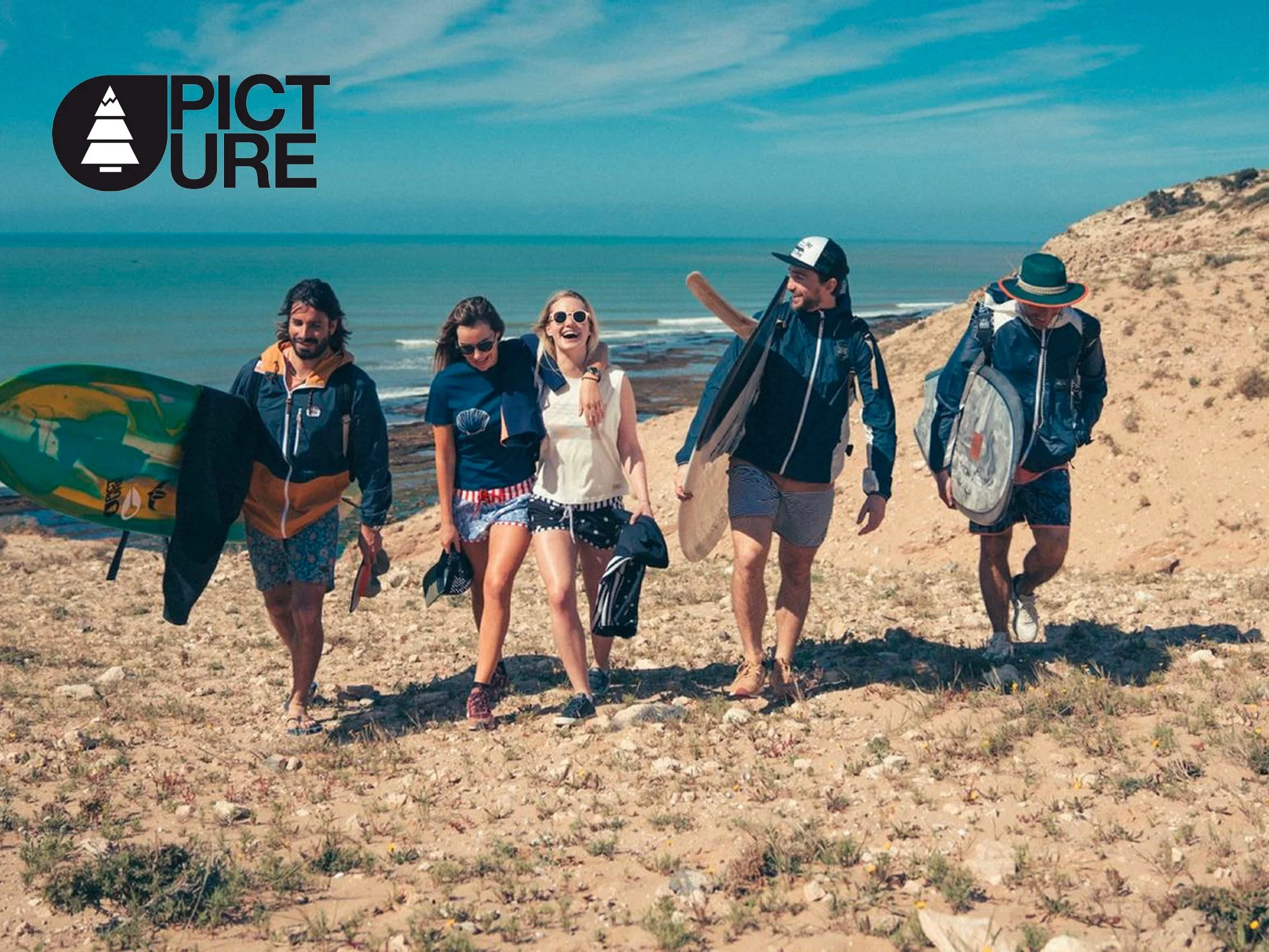 Groupe de cinq jeunes gens en maillot de bain et vêtements décontractés marchant sur la plage avec la mer en fond. Certains portent des sacs, des planches de surf, et sourient.