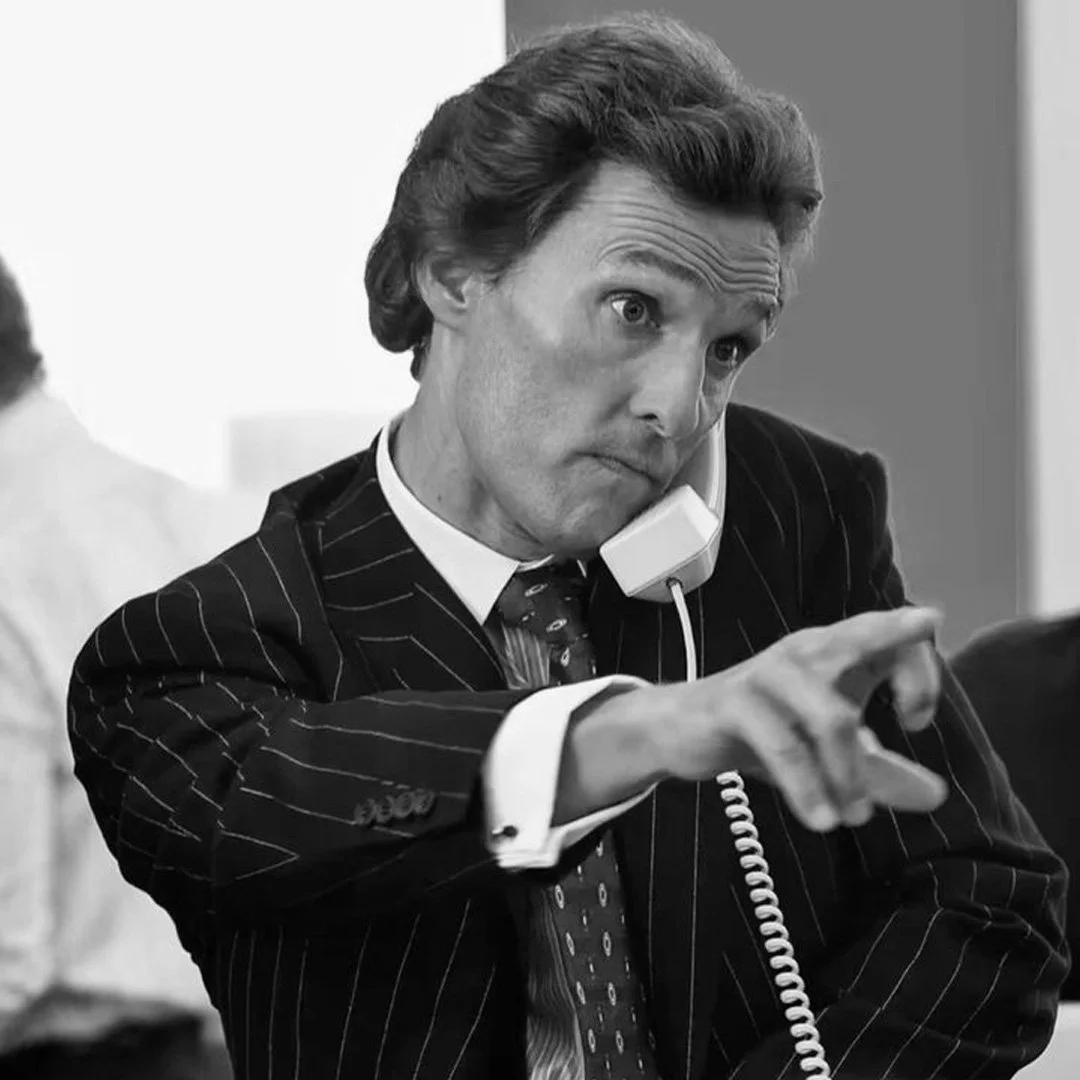 Un homme d'affaires en costume noir à pinstripes, parlant au téléphone avec un look surpris ou sérieux, pointant du doigt.