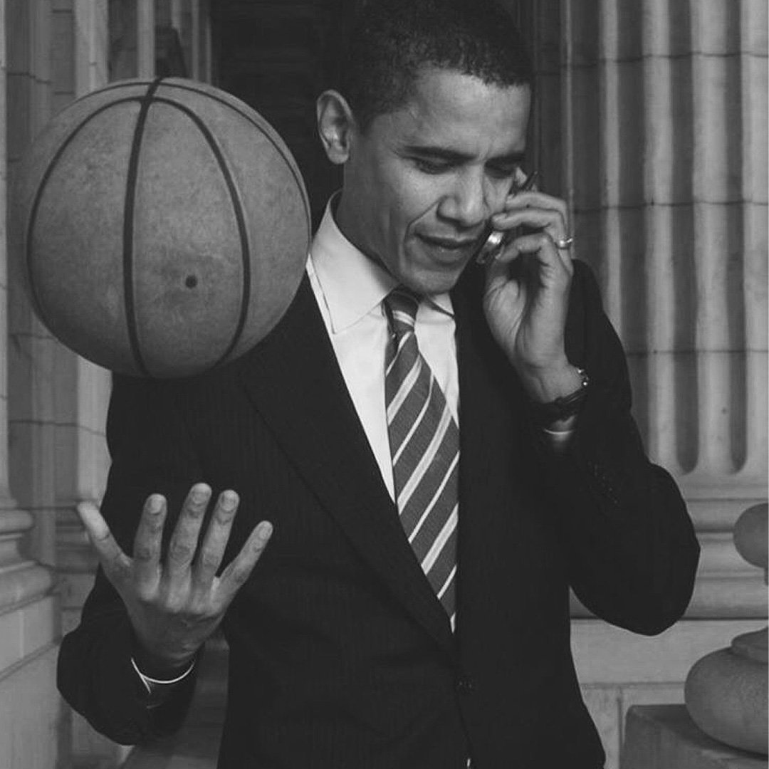 Homme en costume parlant au téléphone avec une main sur le visage, une balle de basket sur son épaule, photo en noir et blanc.