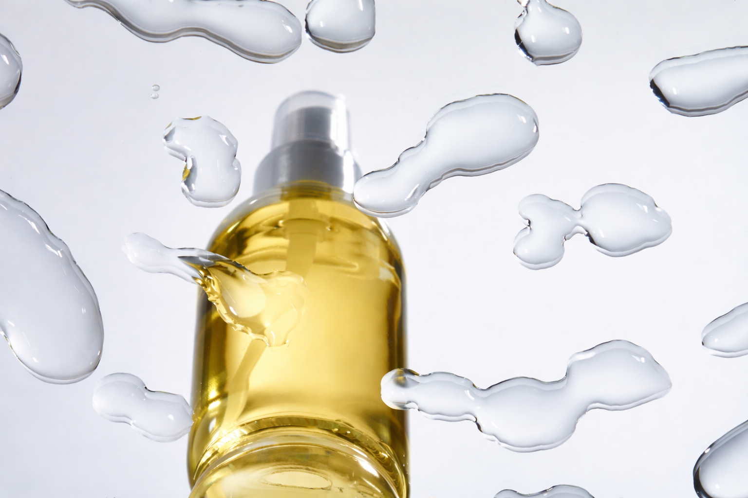 A spray bottle filled with yellow liquid surrounded by splashes of water on a white background.