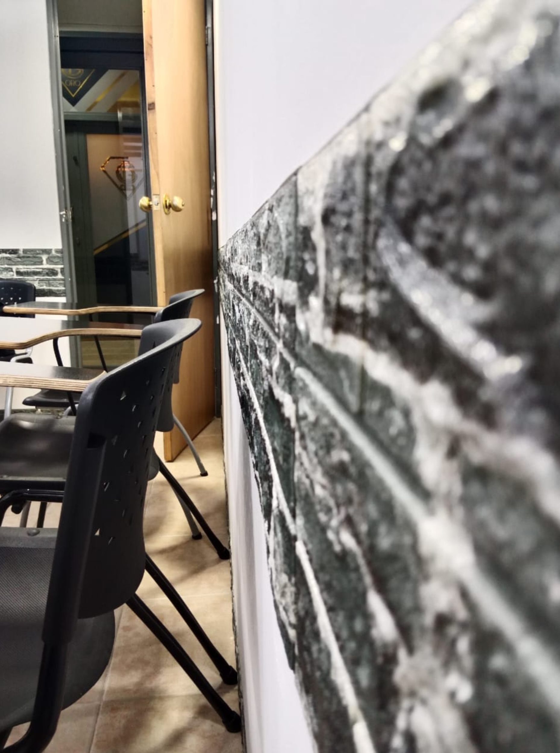Sala de reuniones con sillas negras y mesa de madera, pared con papel tapiz que simula piedra y puerta de madera con pomo dorado.