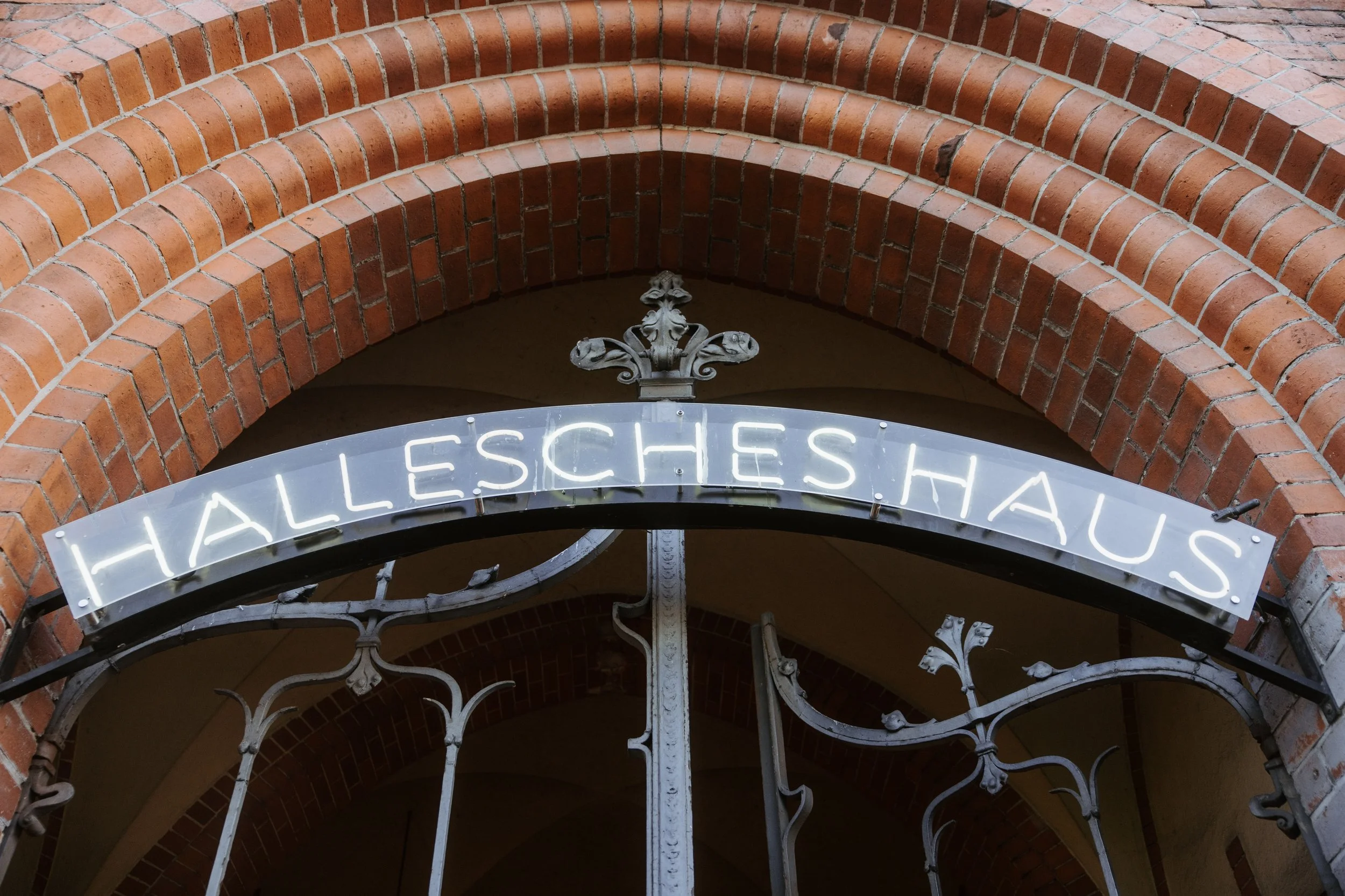 Close-up of an arched brick entrance with a wrought iron gate and a partial white neon sign displaying the word 'Hallesches.'