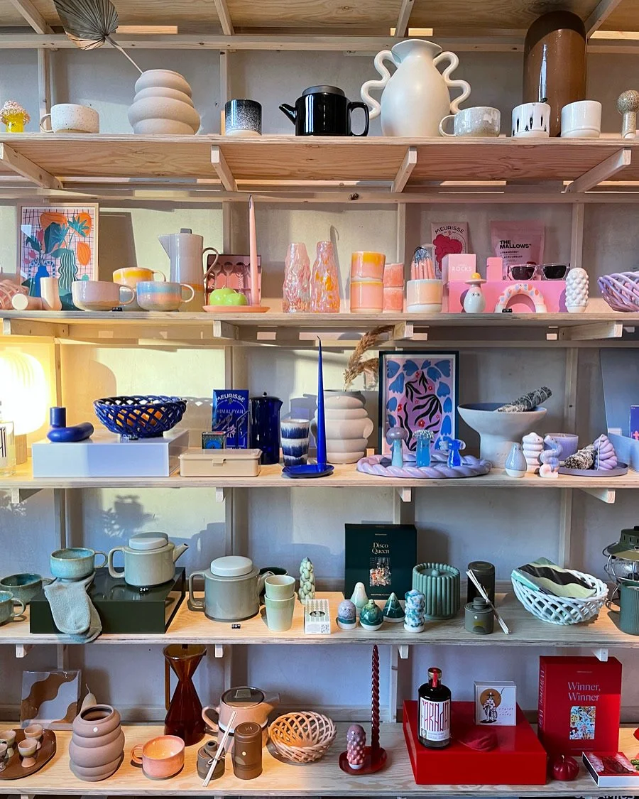 Shelves displaying various colorful ceramics, vases, bowls, mugs, and decorative objects in a store or display setting.