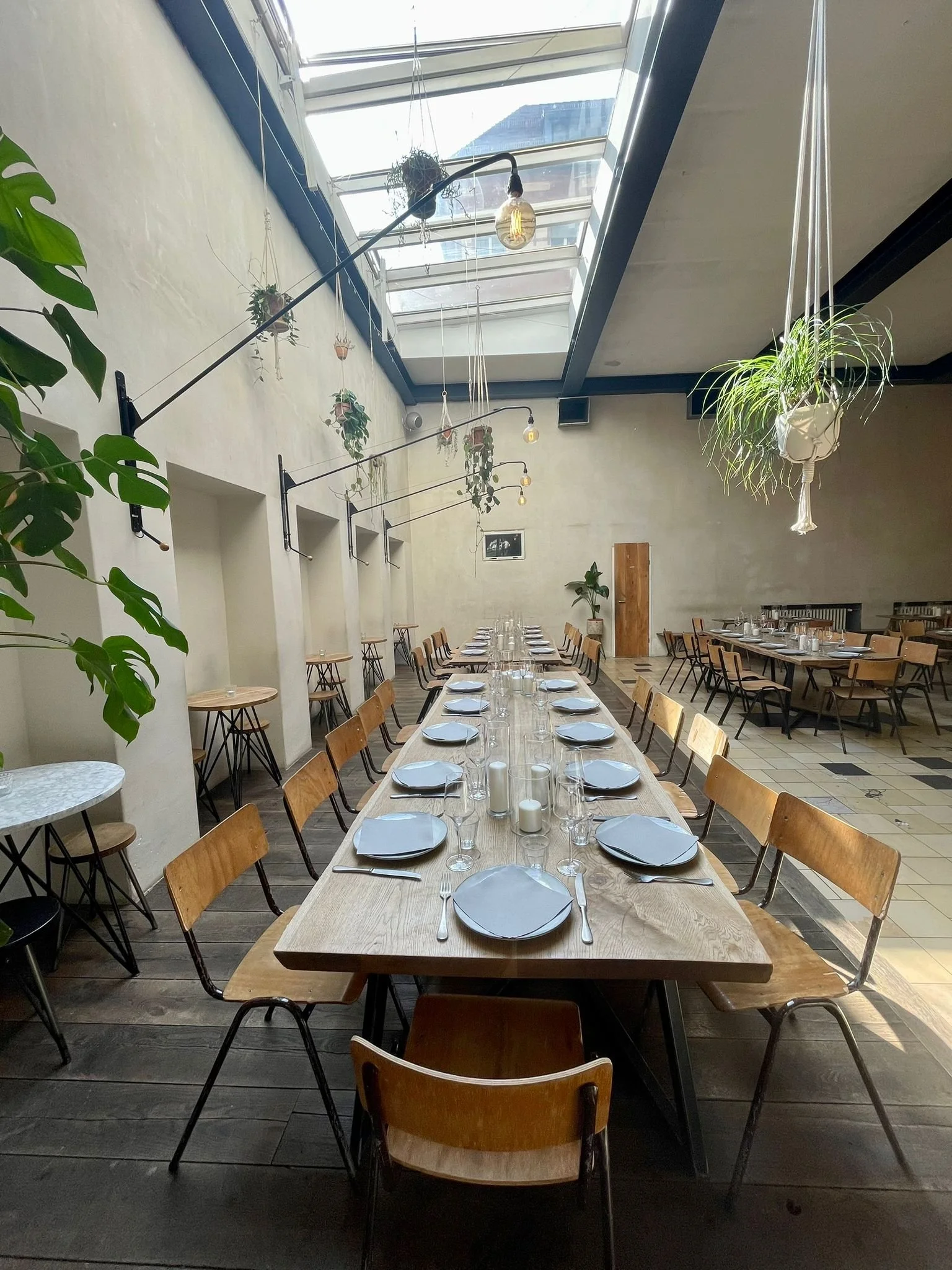 A decorated dining table set for a meal in a bright, modern restaurant with a skylight ceiling and hanging plants.