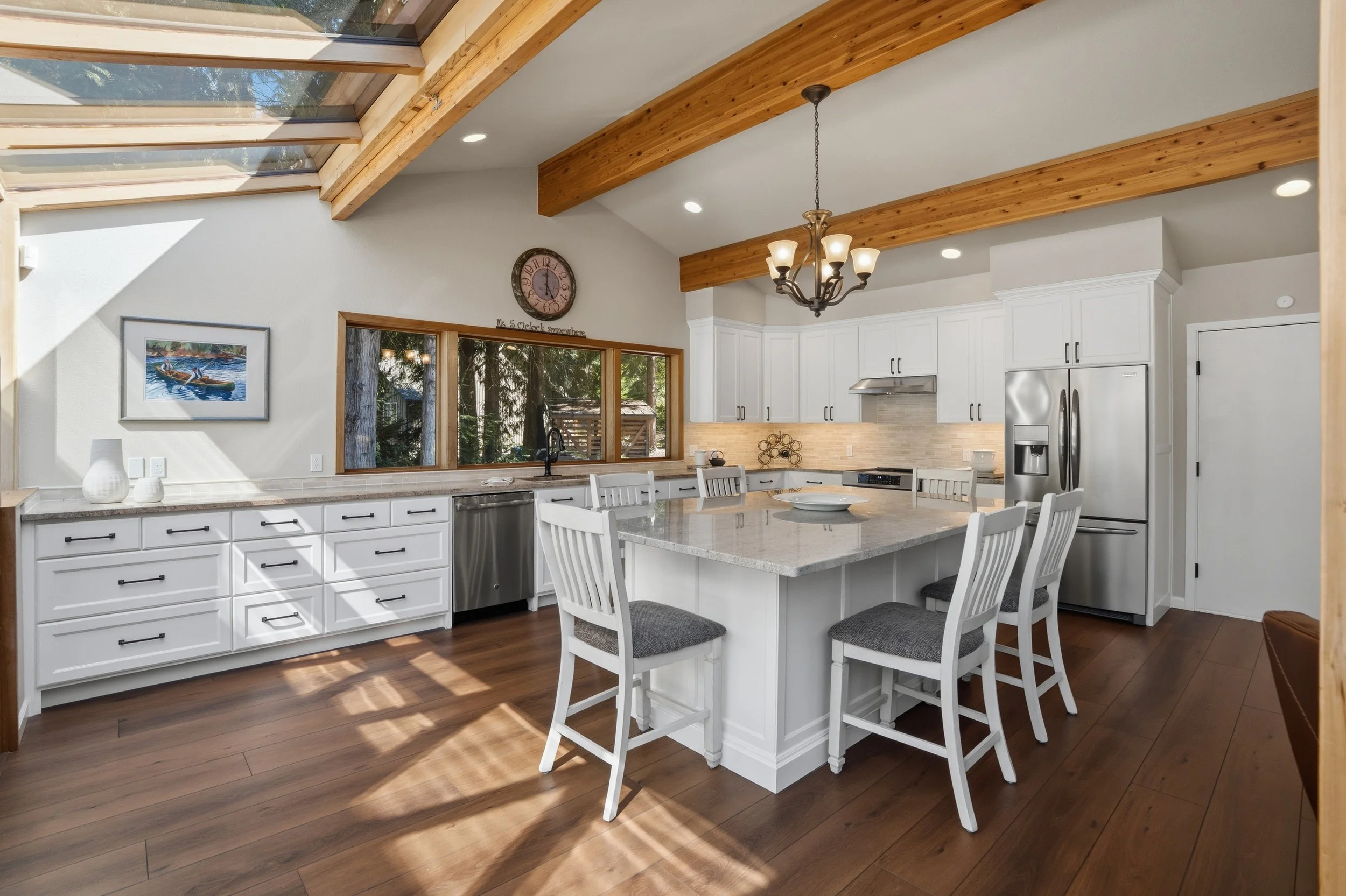 Modern kitchen with white cabinets, stainless steel appliances, large island with seating, wooden floors, and a skylight ceiling.