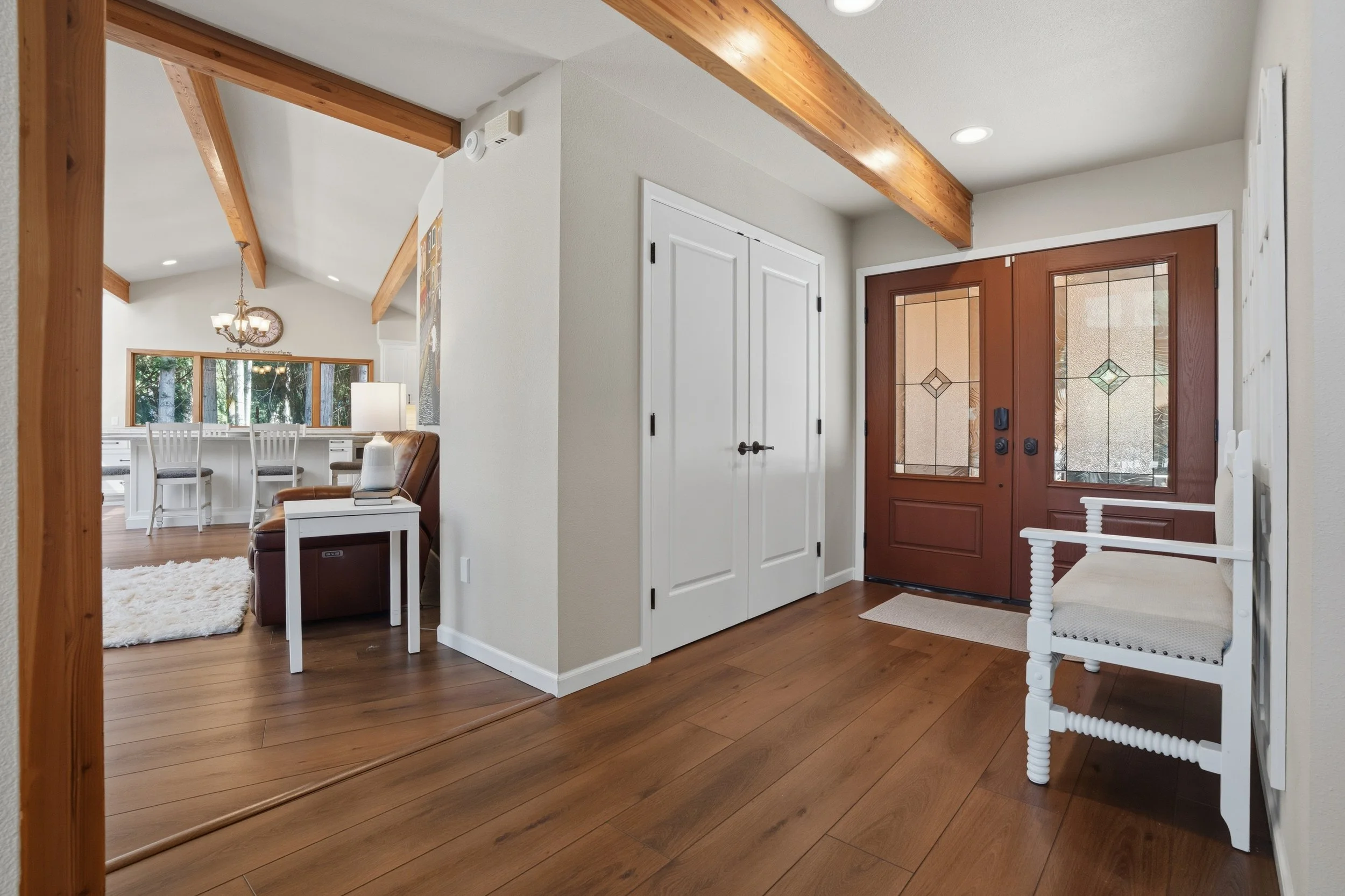 Entryway with wooden flooring, a white bench, a double white closet door, and a wooden front door with decorative glass panels.