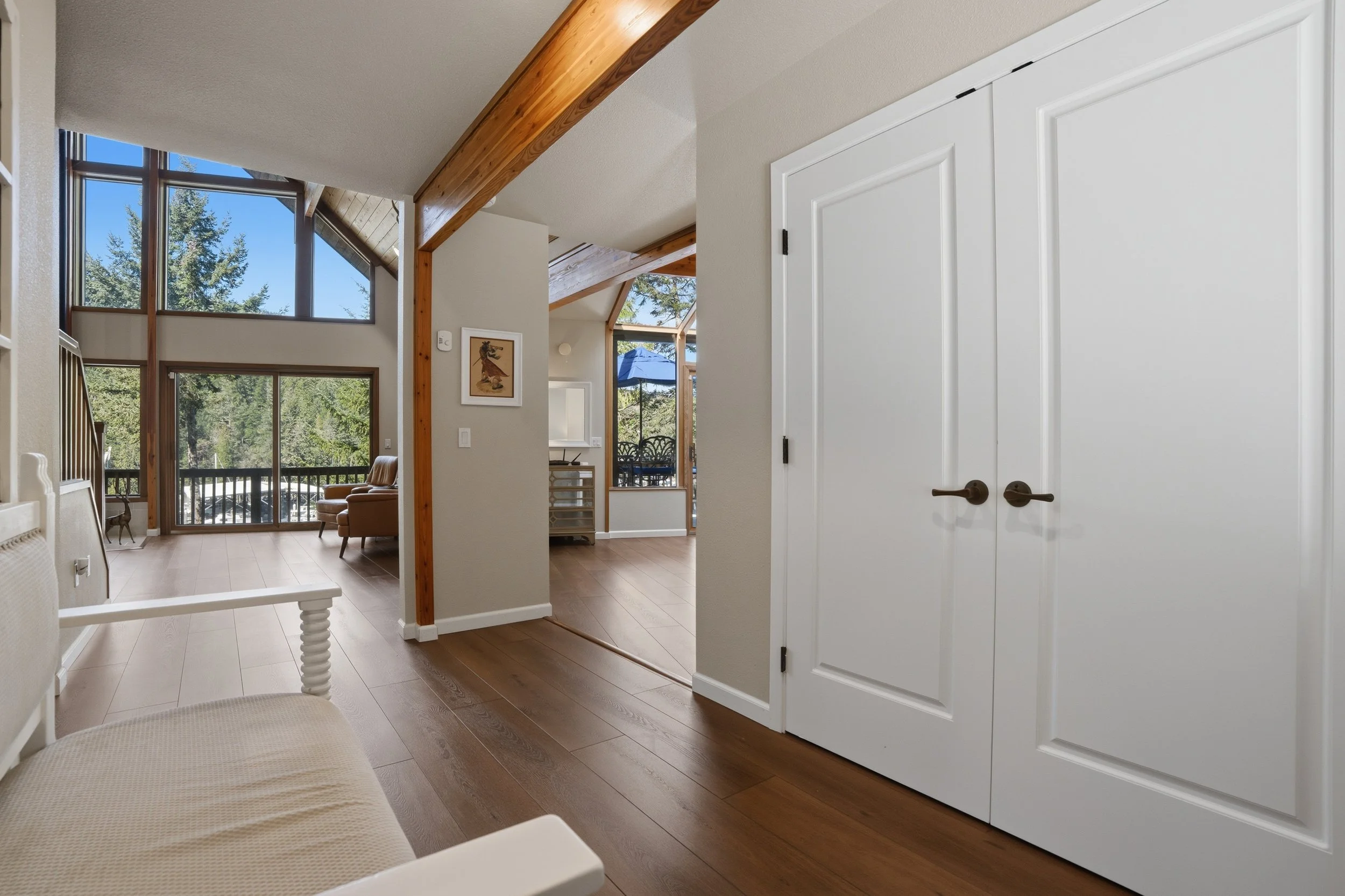 Interior of a modern home with a high vaulted ceiling, large windows providing natural light, wooden accents, and a view of trees outside.