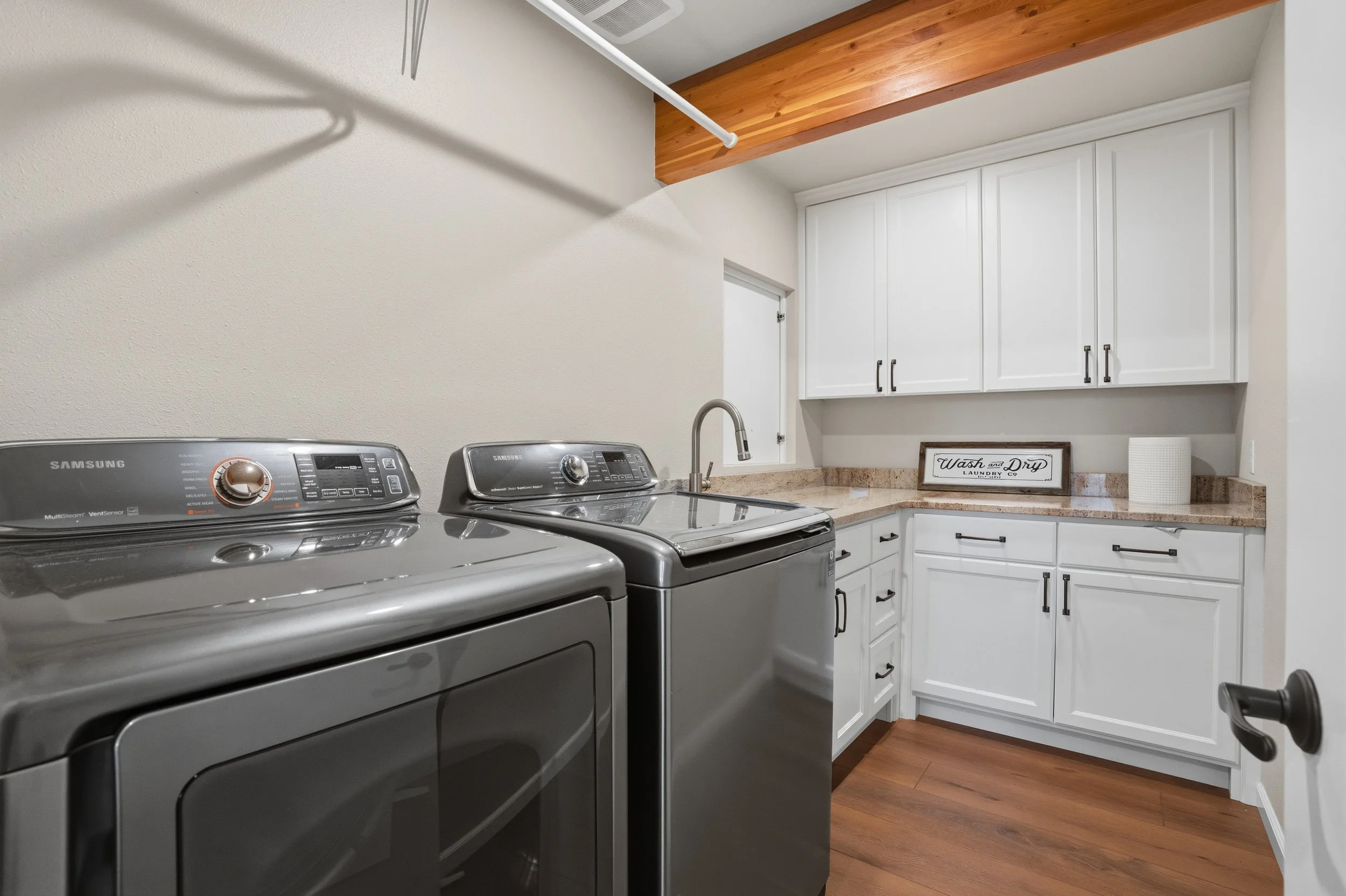 Laundry room with white cabinets, a granite countertop, a washing machine, a dryer, and a wooden floor.
