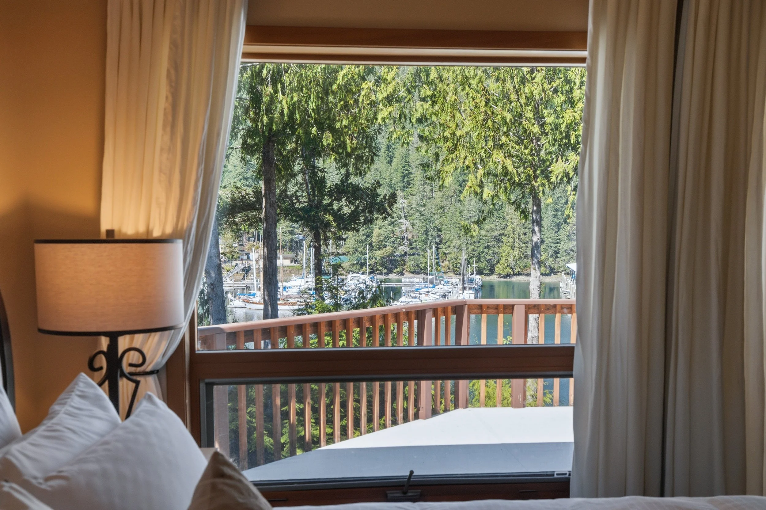 View from a bedroom window overlooking a marina with boats, surrounded by tall green trees.