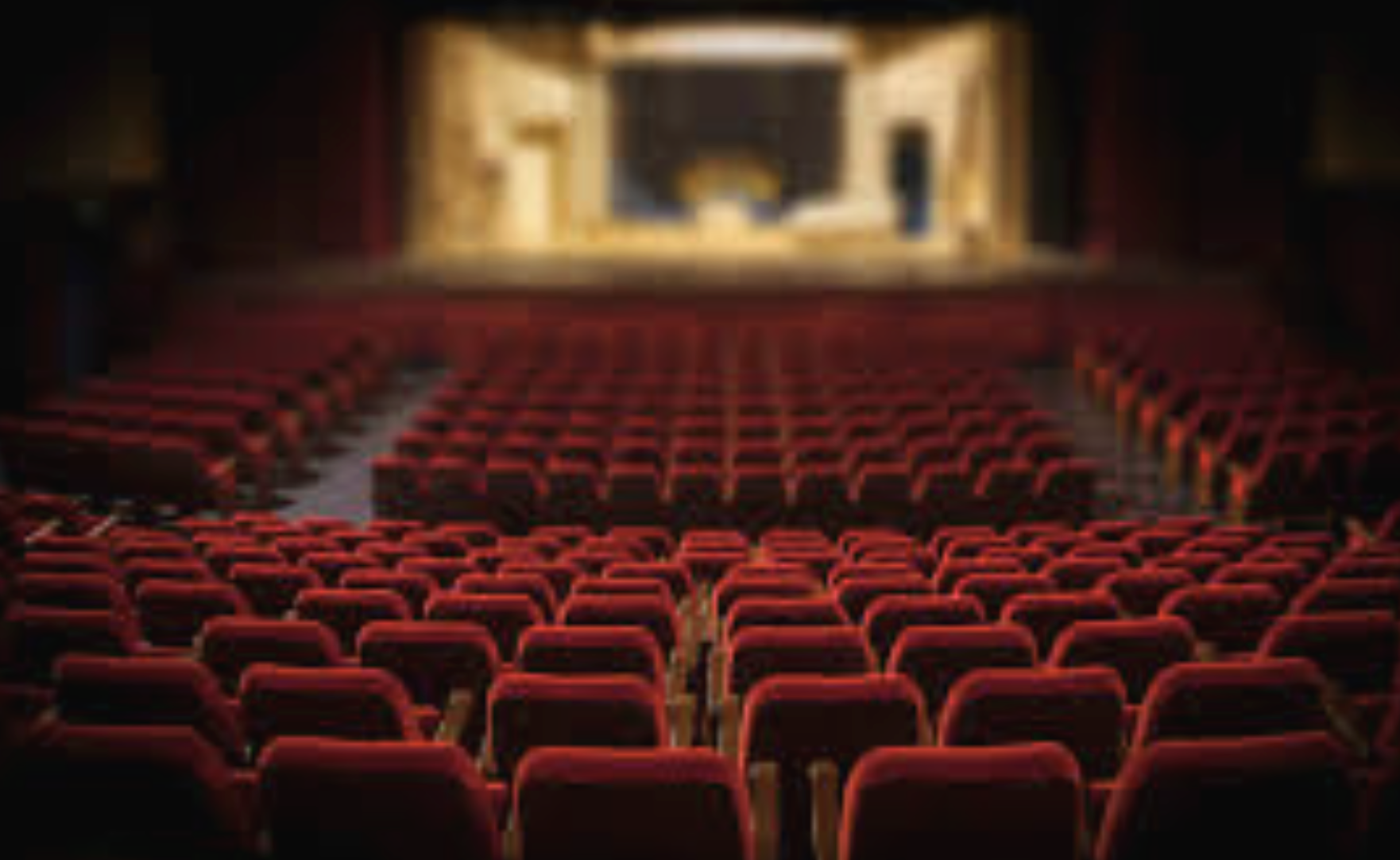 Empty theatre with red velvet seats and a stage with a golden curtain.