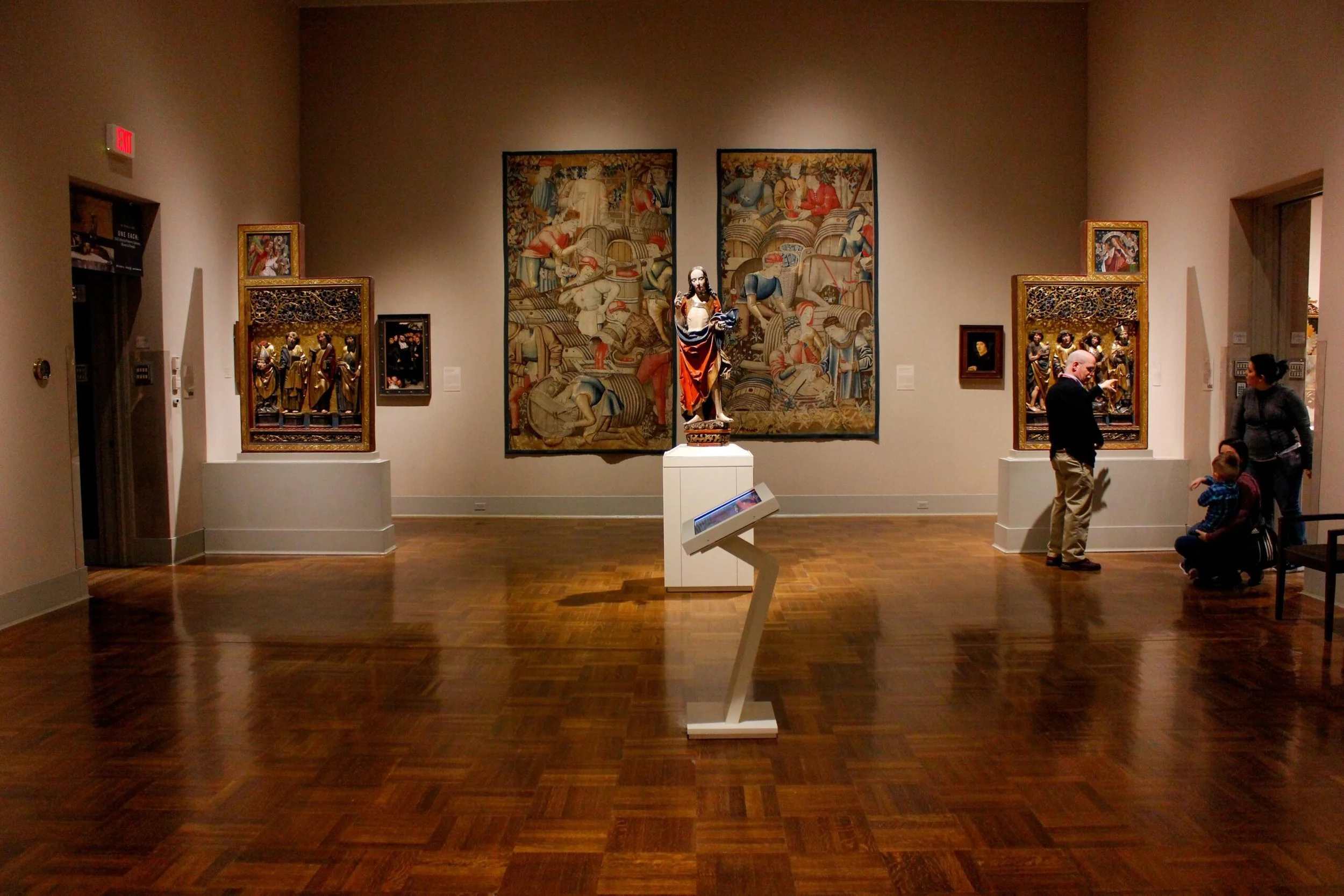Museum gallery with paintings and sculptures, including a central statue and visitors observing the artworks.