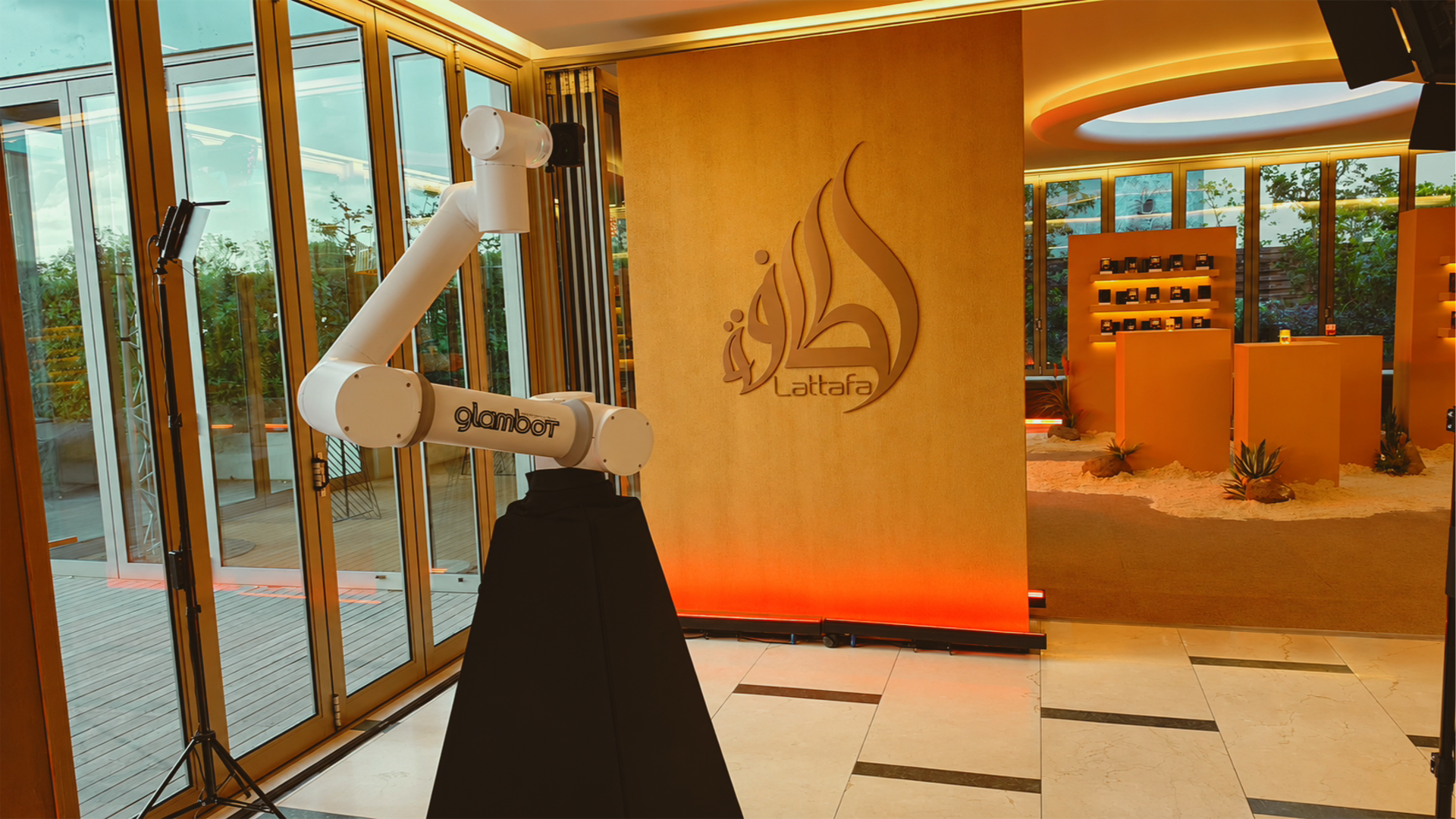 Interior of a modern space with a large robotic arm labeled 'glambot' near glass doors, a wall with the 'Lattafa' logo, and a reception or display area with small platforms and decorative plants.