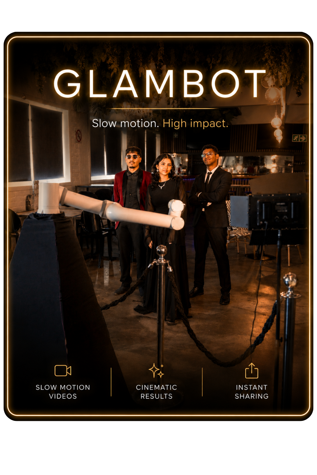 Three people in formal attire standing behind a barrier at a photobooth with a robotic arm, inside a dimly lit modern venue with hanging lights and decorated ceiling, with neon signs and windows in the background.