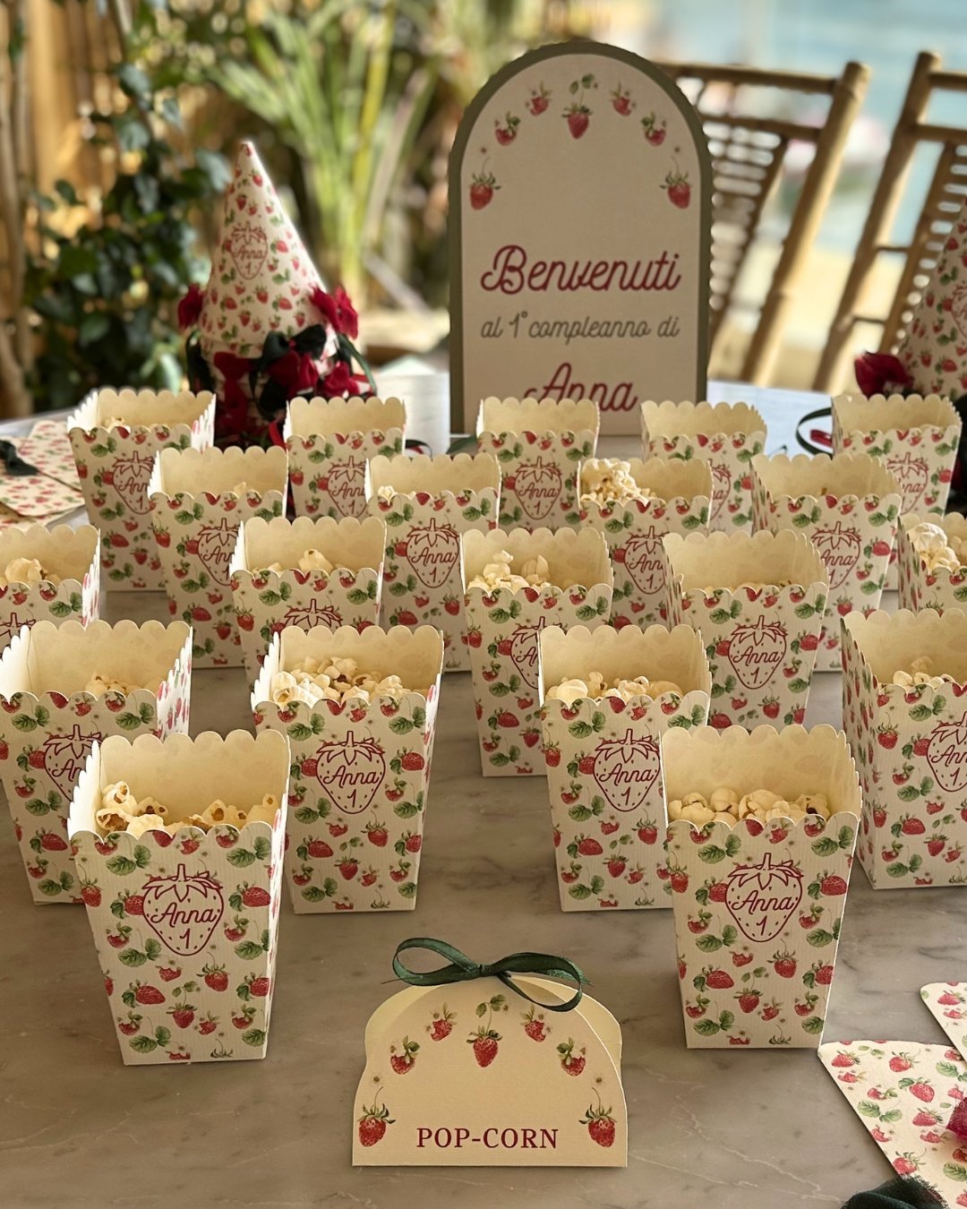 Scatoline porta popcorn personalizzate e cartello di benvenuto per festa a tema fragole, realizzati in carta e coordinati nei dettagli.