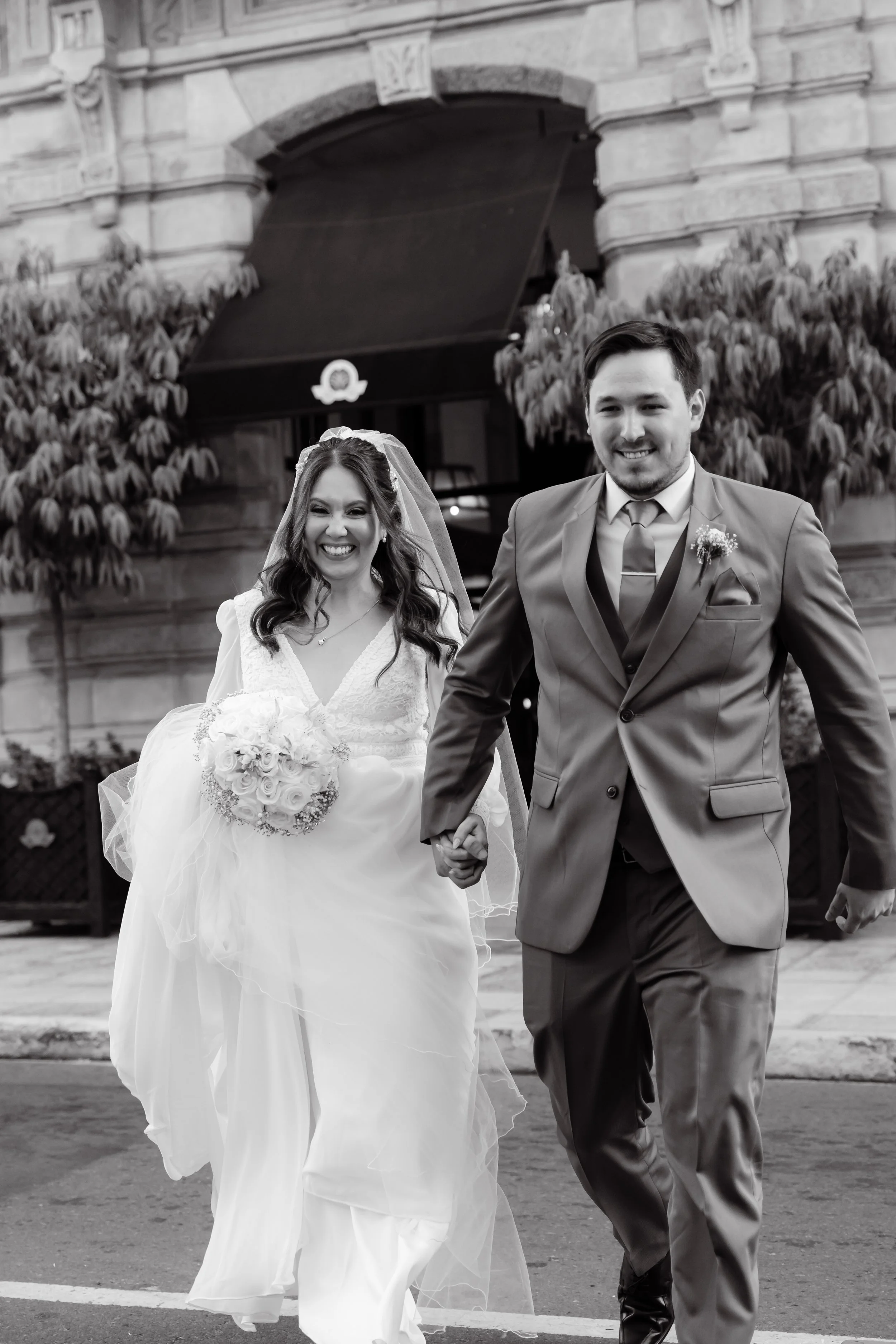 Una pareja de recién casados camina felizmente por la calle, la novia con vestido de novia y ramo, el novio con traje, en una ciudad.