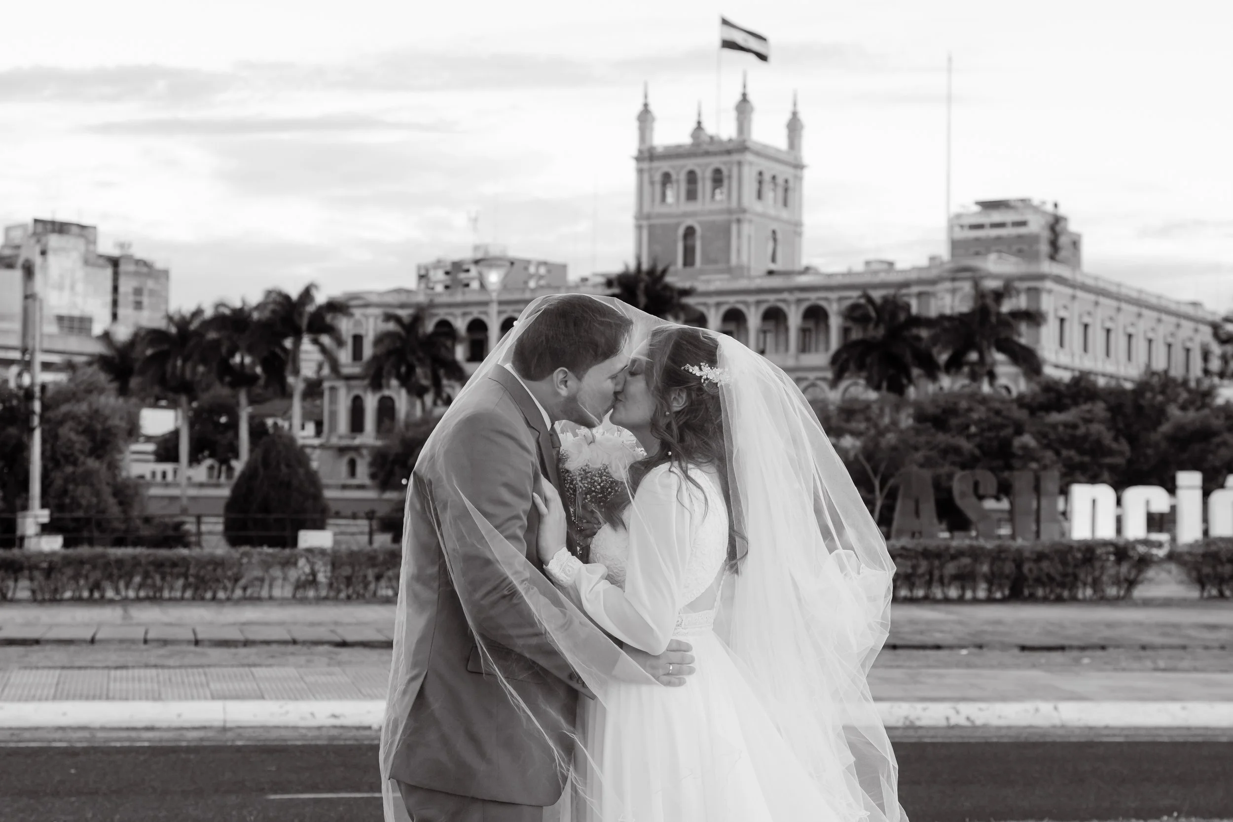 Pareja de recién casados besándose con el ayuntamiento de Lima, Perú, en el fondo, en blanco y negro.