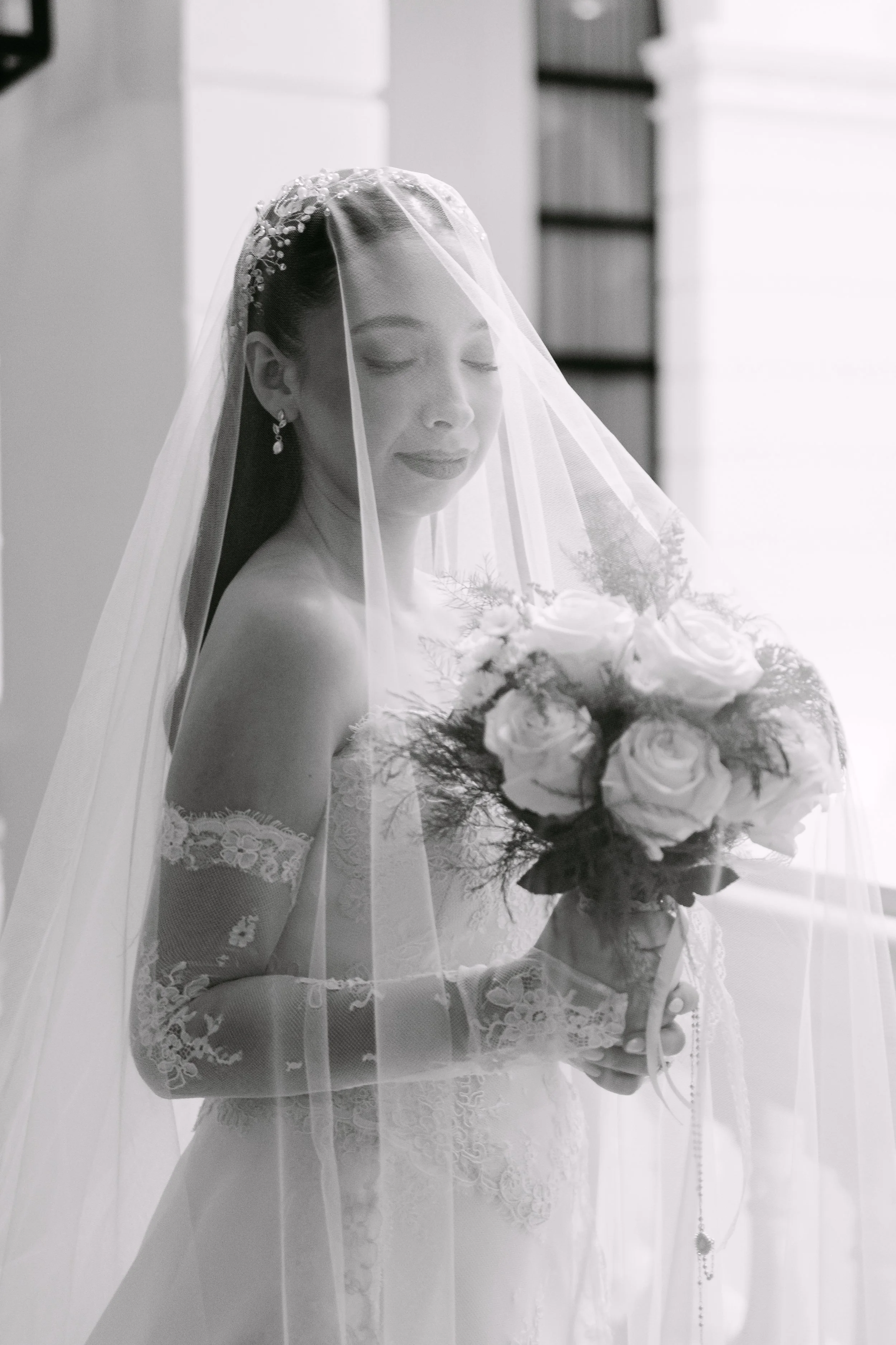 Mujer con vestido de novia, velo y accesorios, sostenido un ramo de rosas en una fotografía en blanco y negro.
