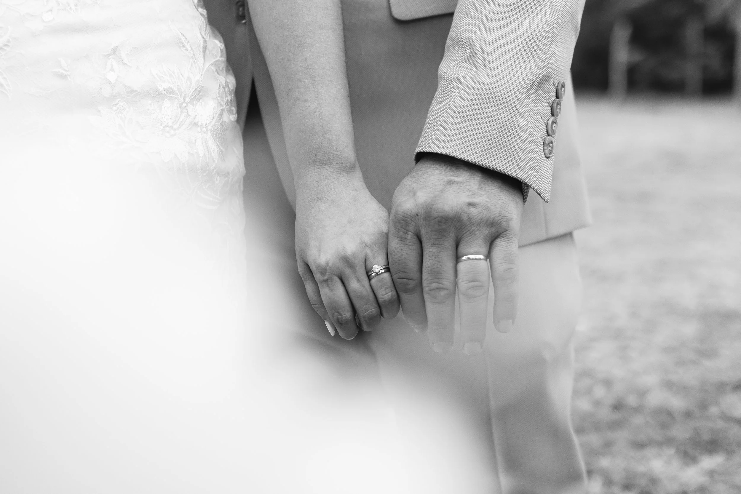 Manos entrelazadas de una pareja casada con anillos en los dedos, en B/N.