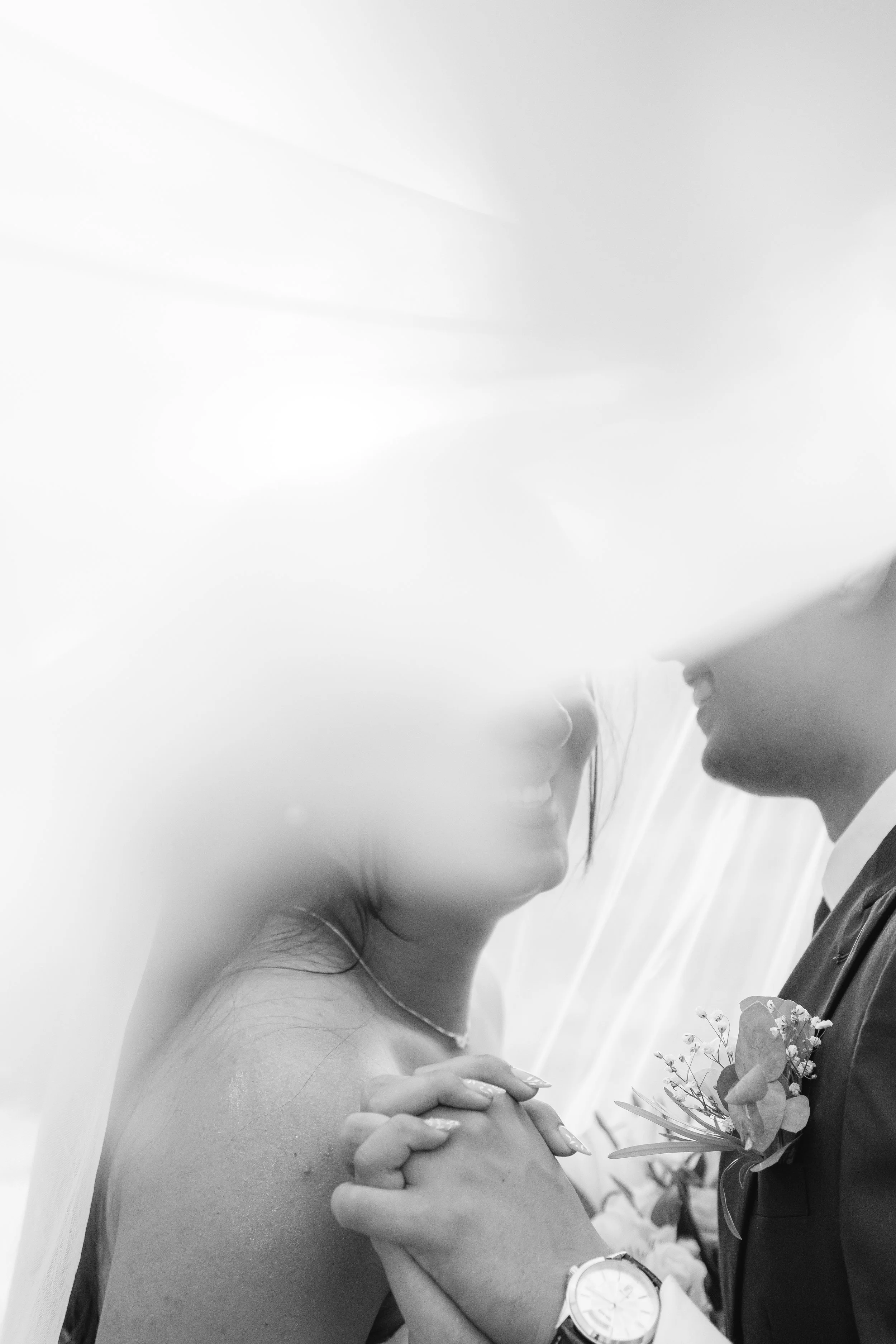 Pareja de novios en una boda, sonriendo y sosteniéndose las manos, en un ambiente romántico.