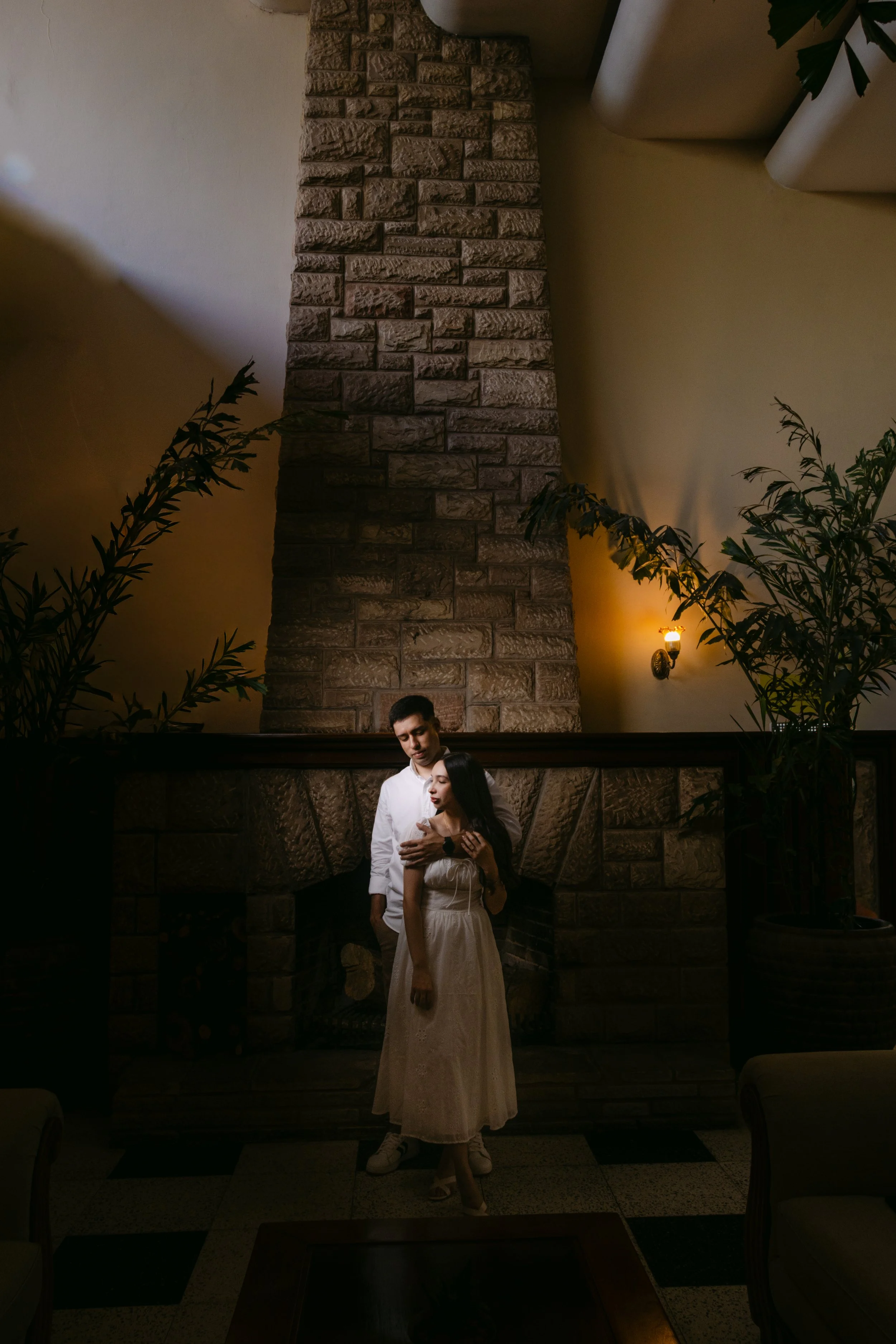 Una pareja en un ambiente interior, en una chimenea con techo de piedra y plants de fondo.