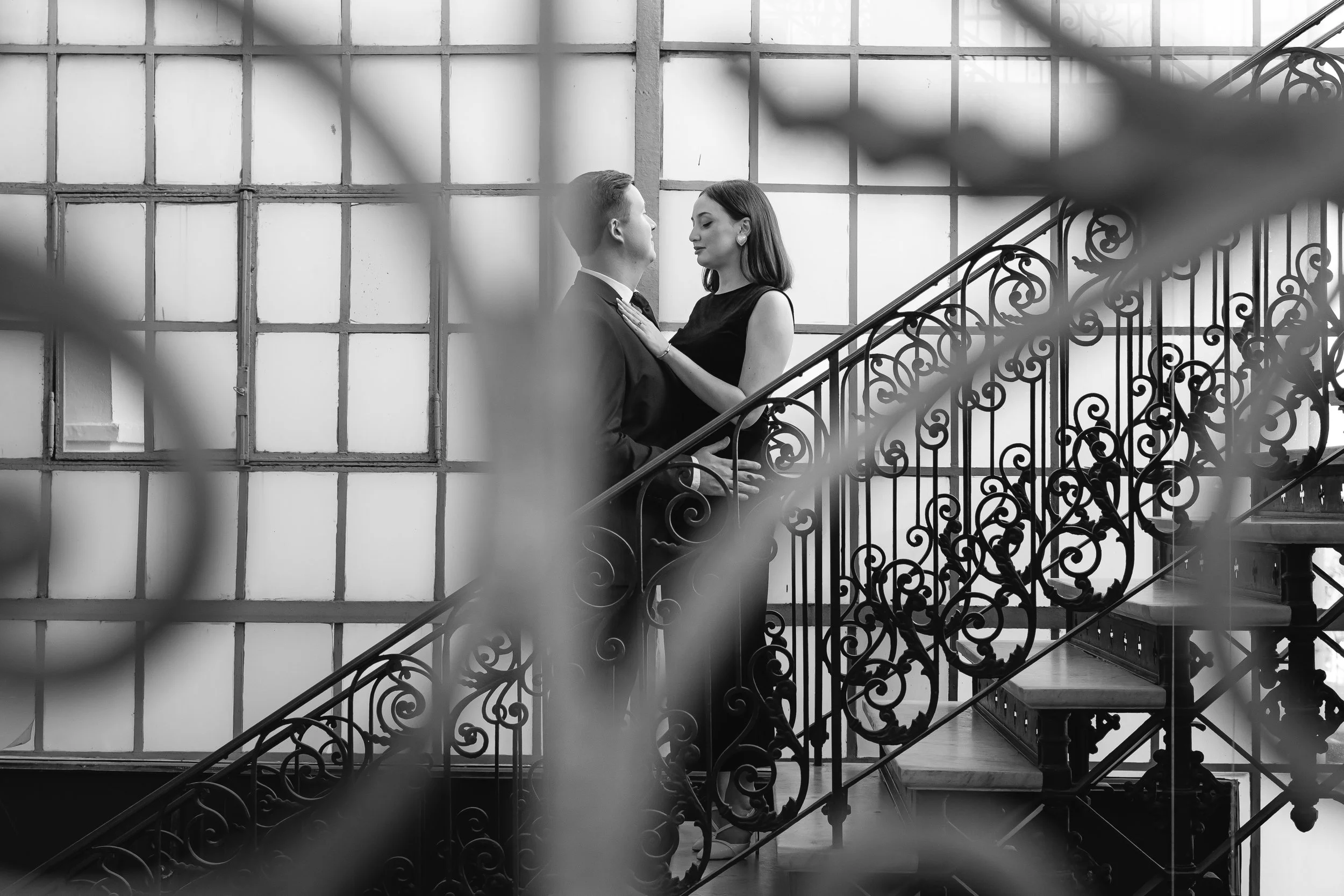 Pareja en un baile romántico en una escalera de hierro, en un entorno elegante y moderno, en blanco y negro.