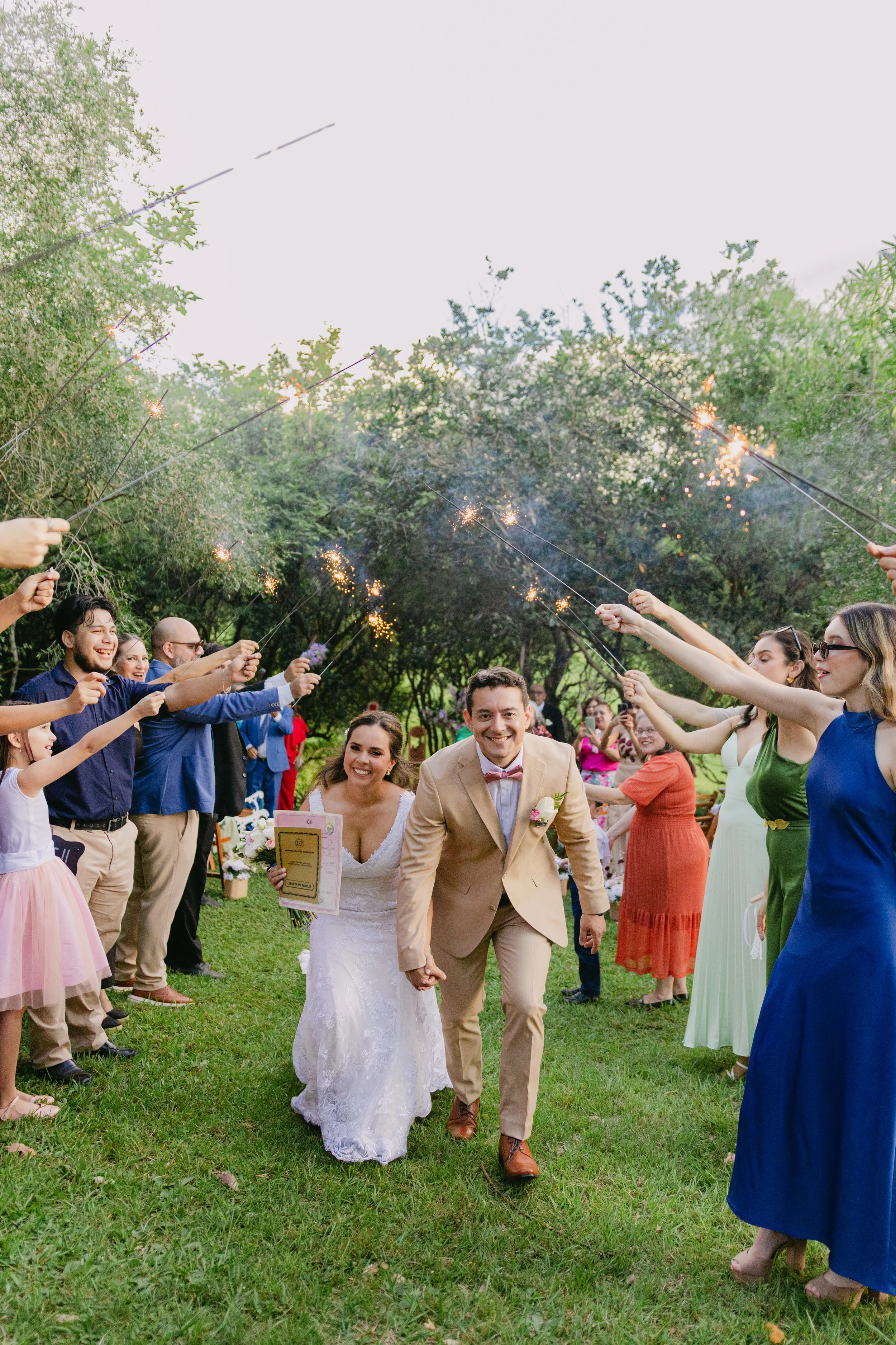 Recien casados caminando entre invitados que sostienen fèbulas con cohetes en un ambiente exterior