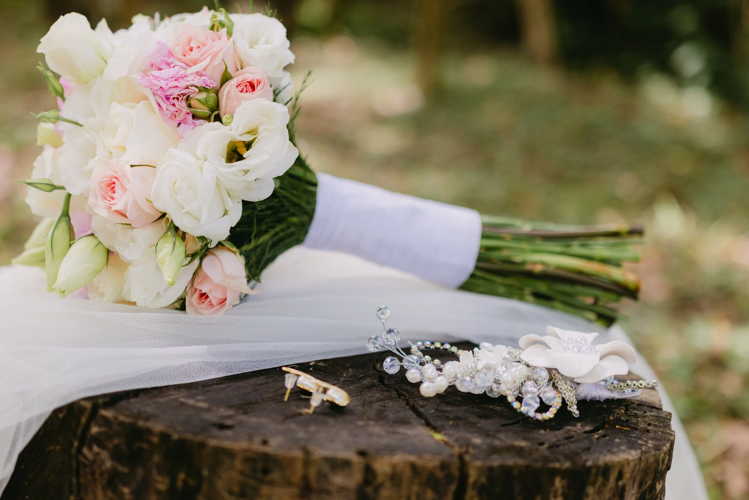 Ramo de flores de boda con rosas blancas y rosas rosadas, decoraciones de joyería y accesorios sobre un tronco de árbol
