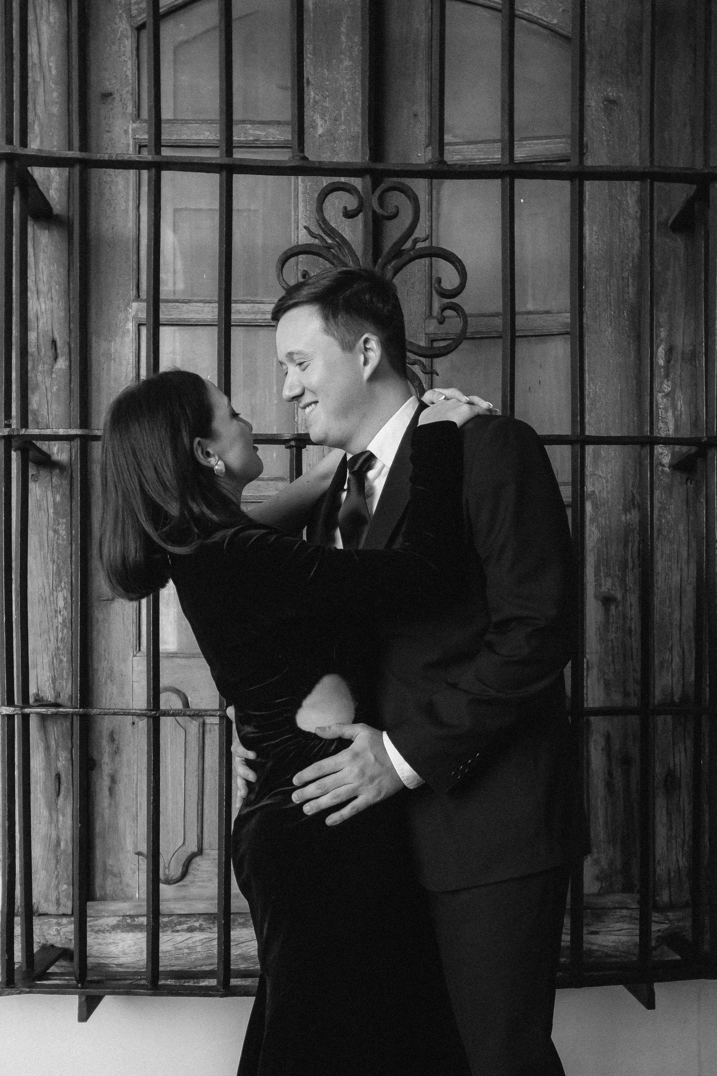 Pareja sonriendo y abrazándose adentro de una jaula de metal con paredes de madera, en blanco y negro.