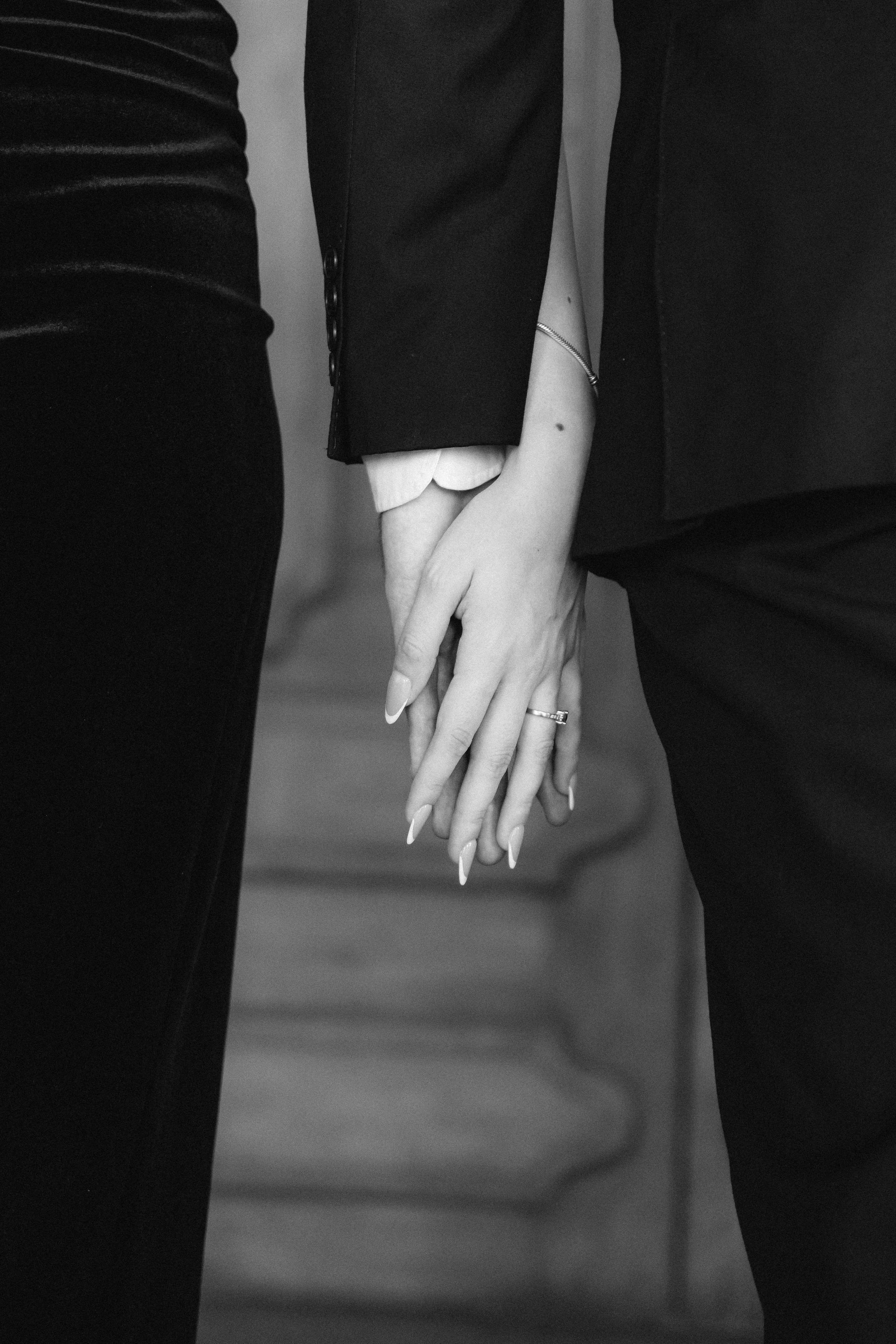 Dos personas entrelazando sus manos, vestidas con ropa formal, en un ambiente en blanco y negro.