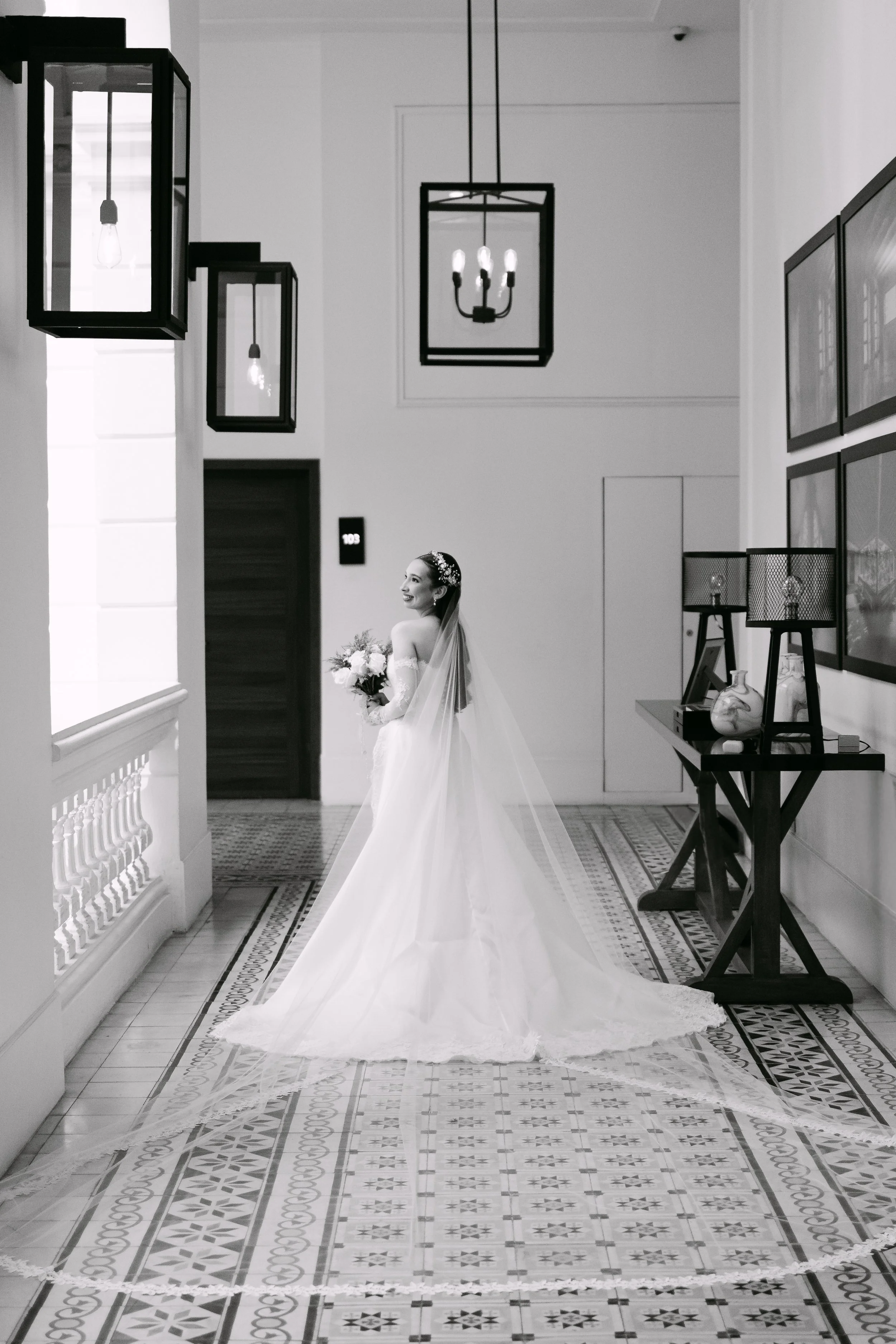 Mujer con vestido de novia y ramo de flores en un pasillo con iluminación de lámparas de techo y decoración moderna.
