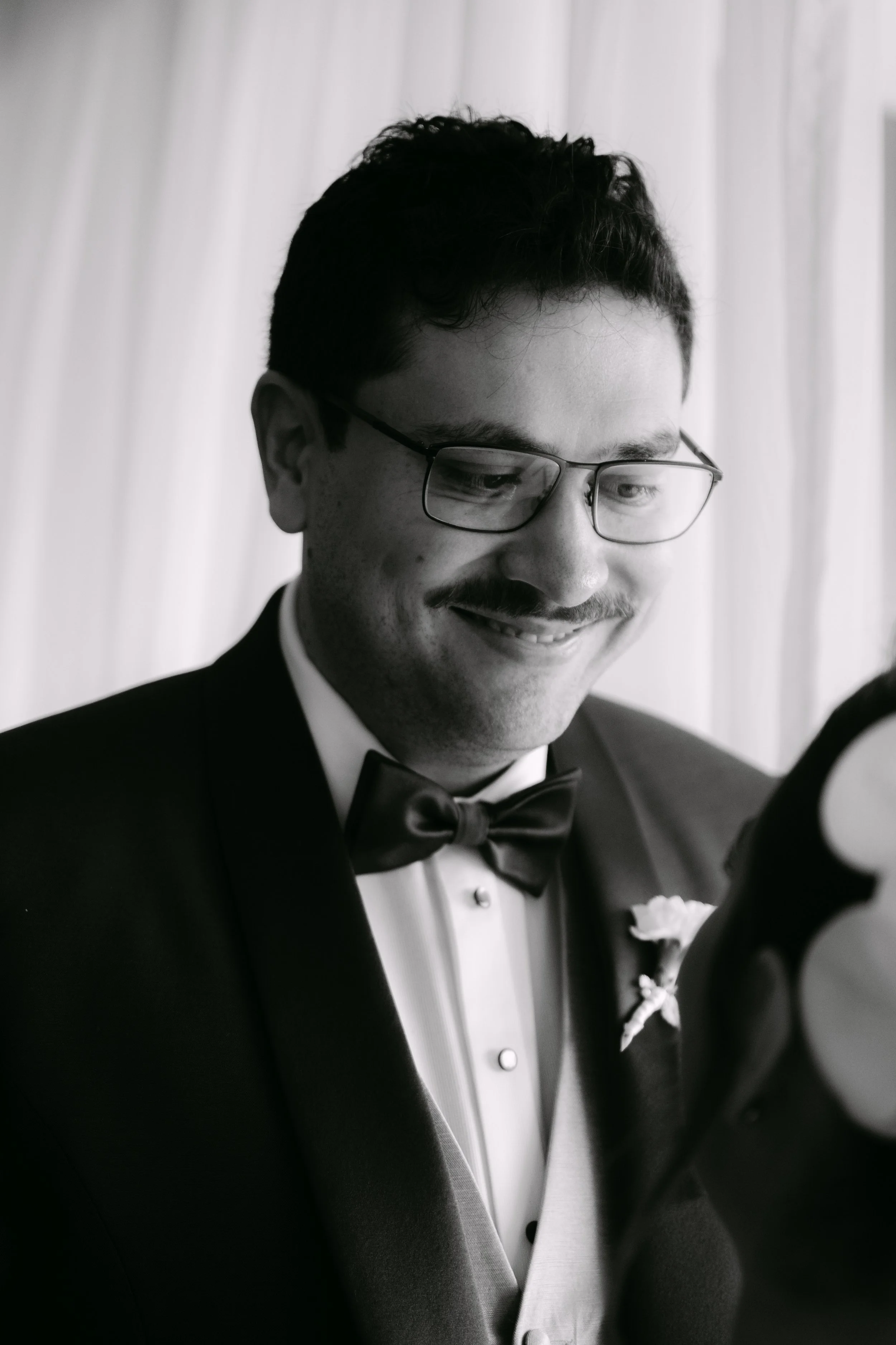 Hombre con peinado oscuro, barba y gafas, vestido con un esmoquin negro y una pajarita, sonriendo en un evento formal.