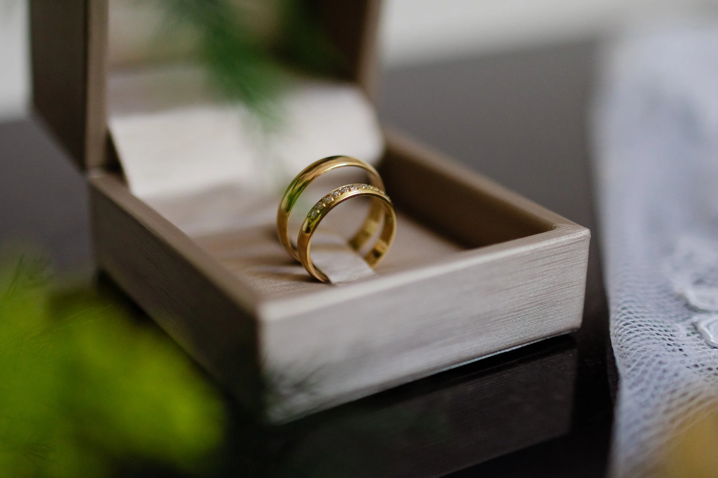 Dos anillos de oro, uno con piedras brillantes, colocados en una caja de joyería de color beige
