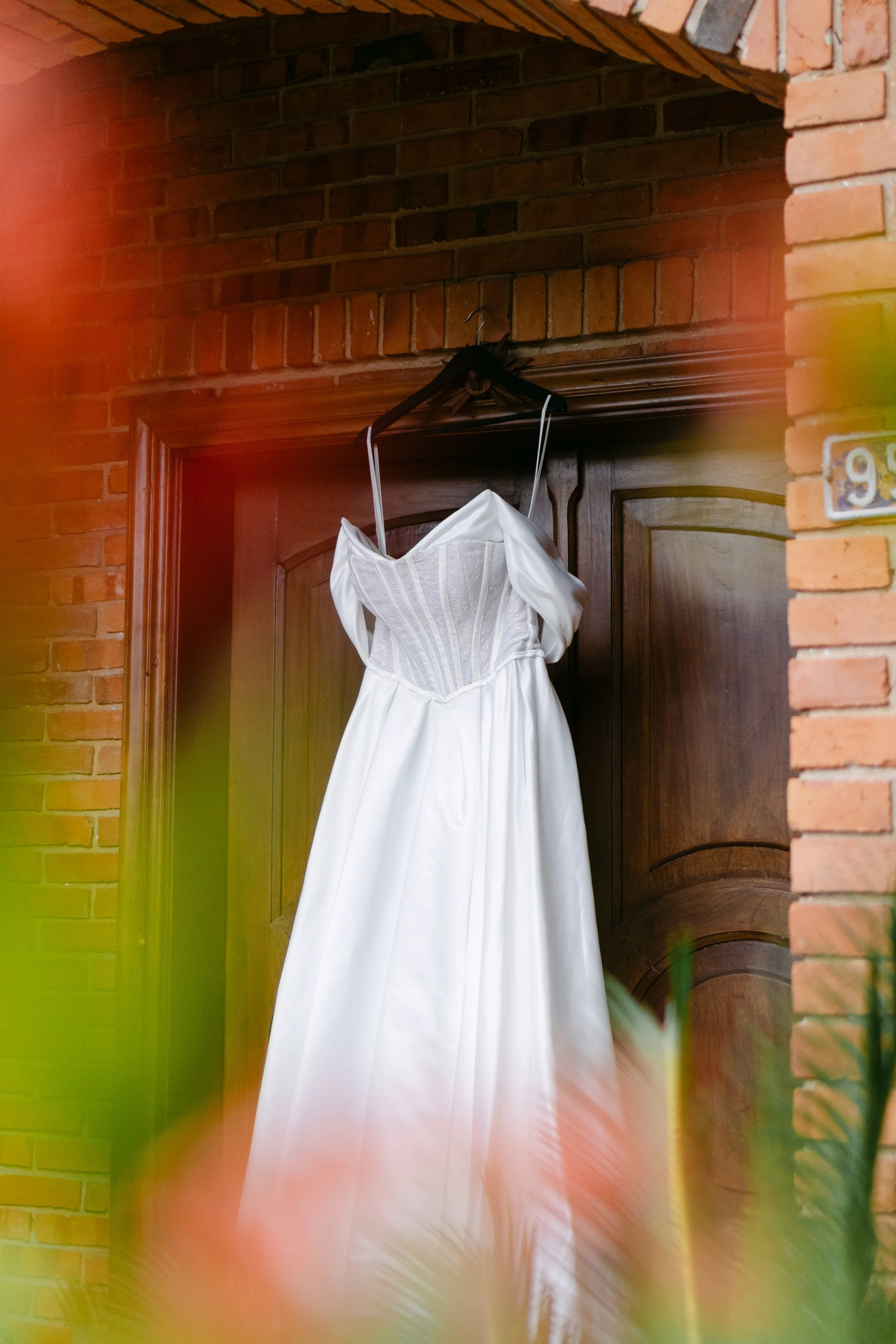 Un vestido de novia blanco colgado en un perchero sobre una puerta de madera, en un espacio de paredes de ladrillo.