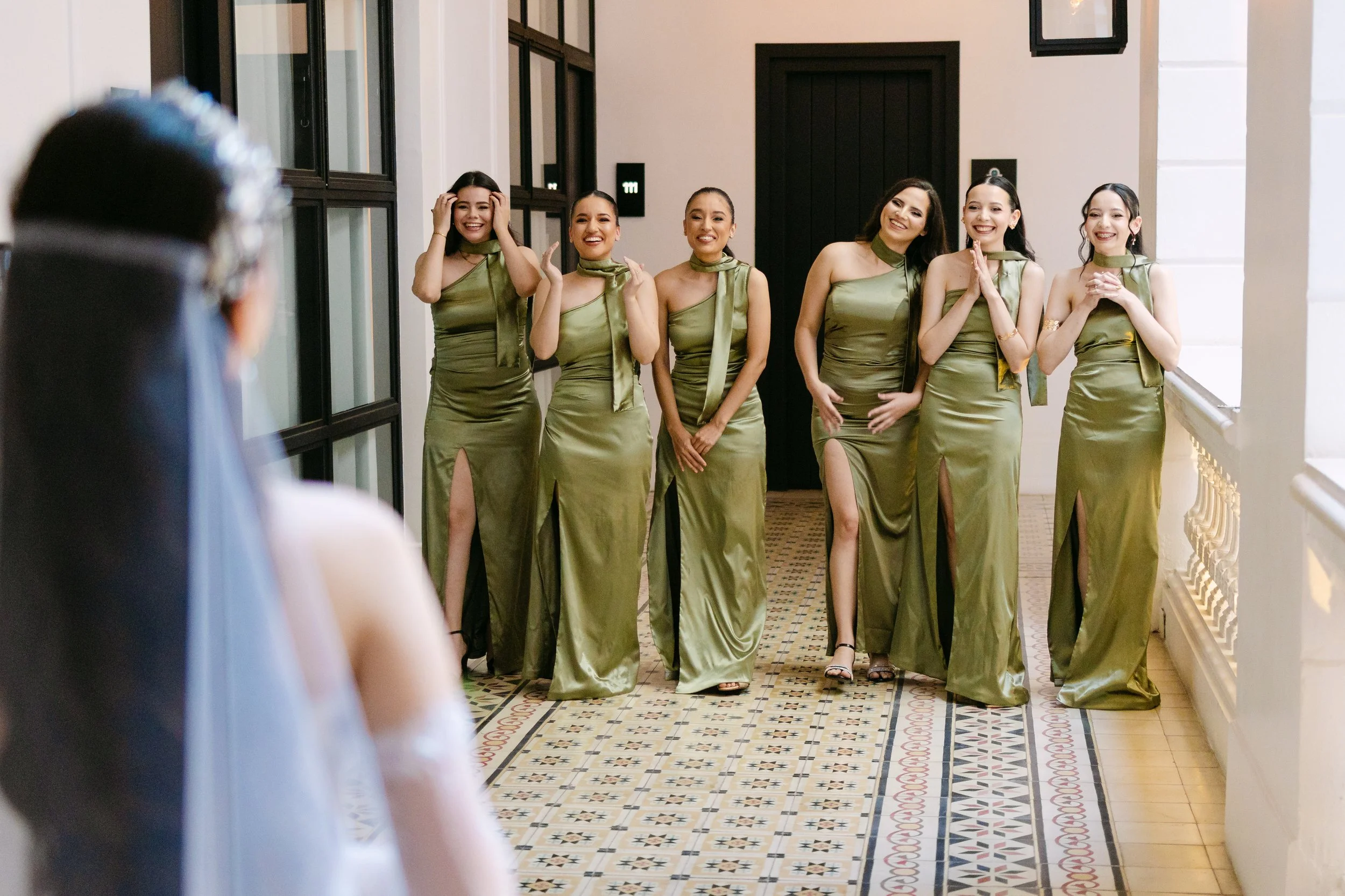 Grupo de seis mujeres vestidas con vestidos largos de color verde raya, posando en un pasillo, sonriendo y aparentando estar preparadas para un evento especial.