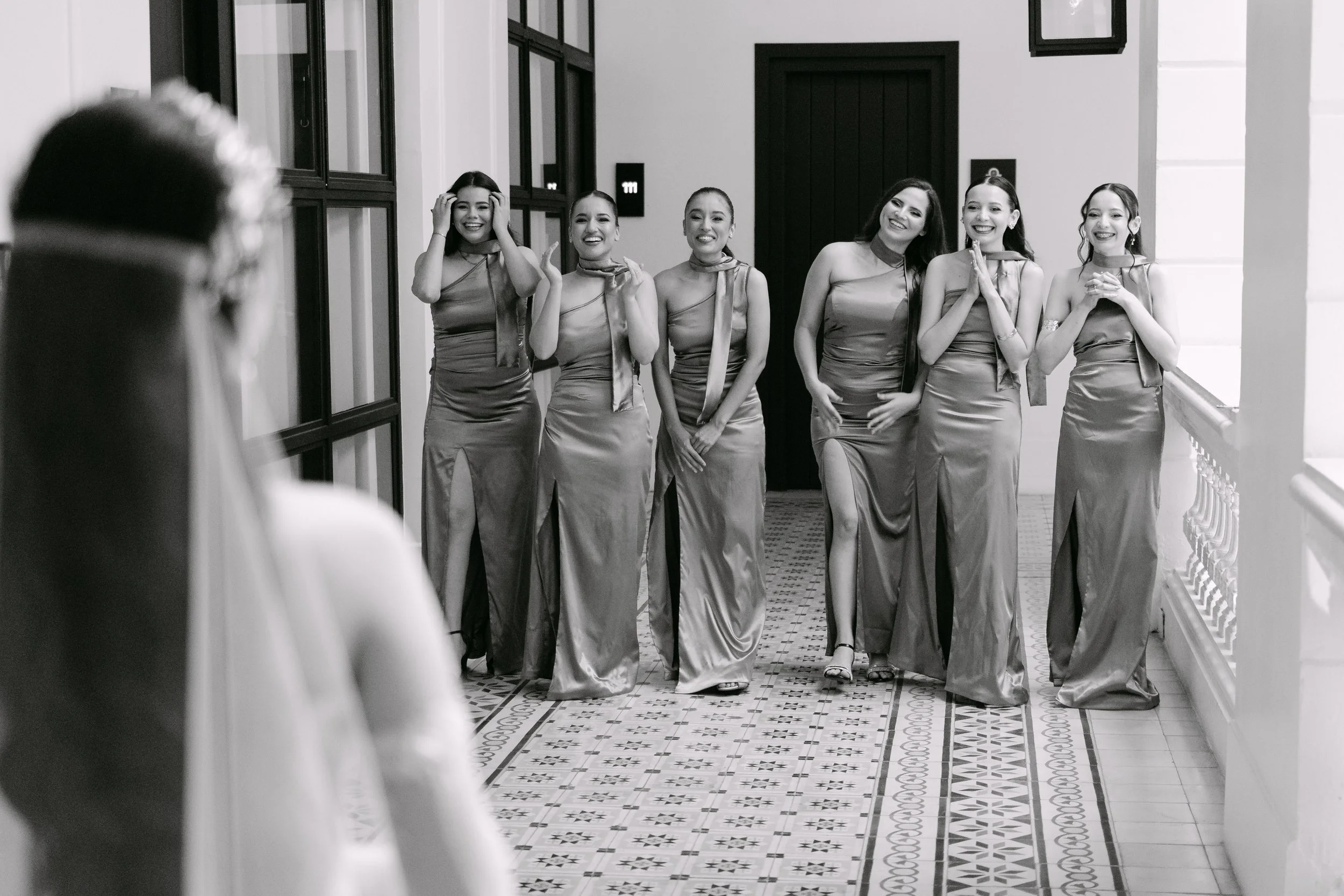 Grupo de mujeres vestidas con vestidos largos de seda en un pasillo, riendo y posando para la cámara.