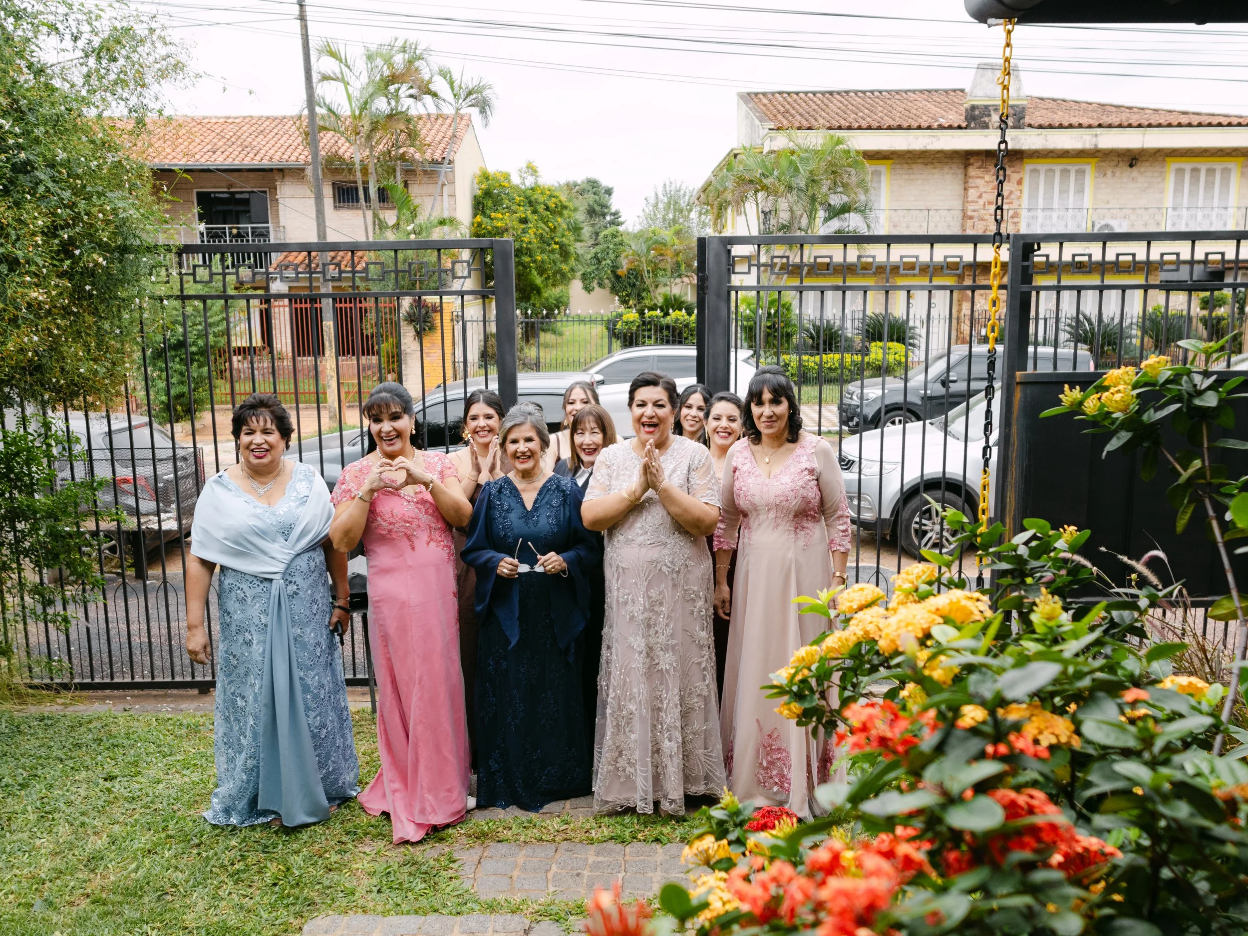 Grupo de mujeres sonriendo y posando en un entorno exterior con jardín y casas al fondo.