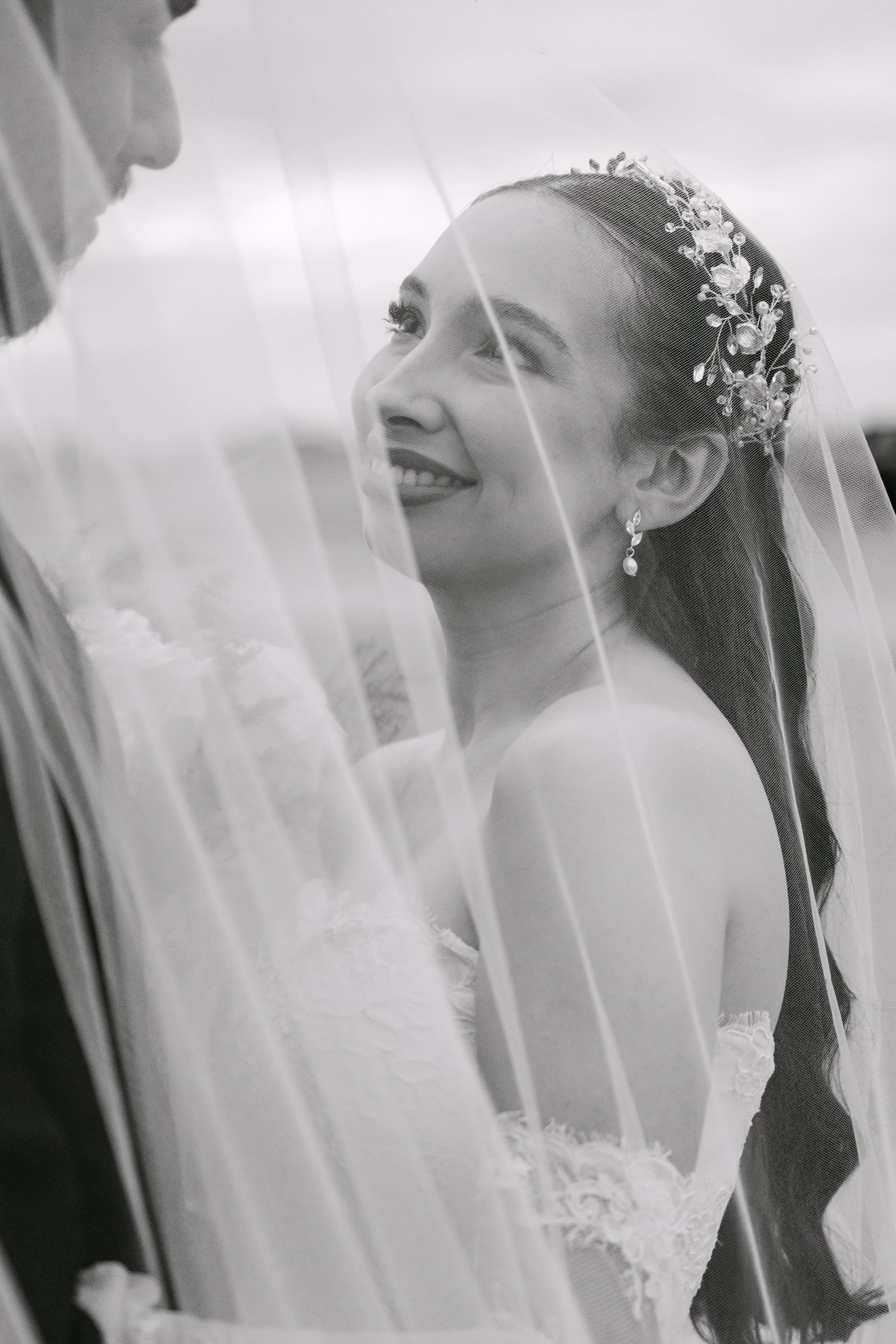 Mujer de novia sonriendo con velo y pendientes vistas a través de una ventana.