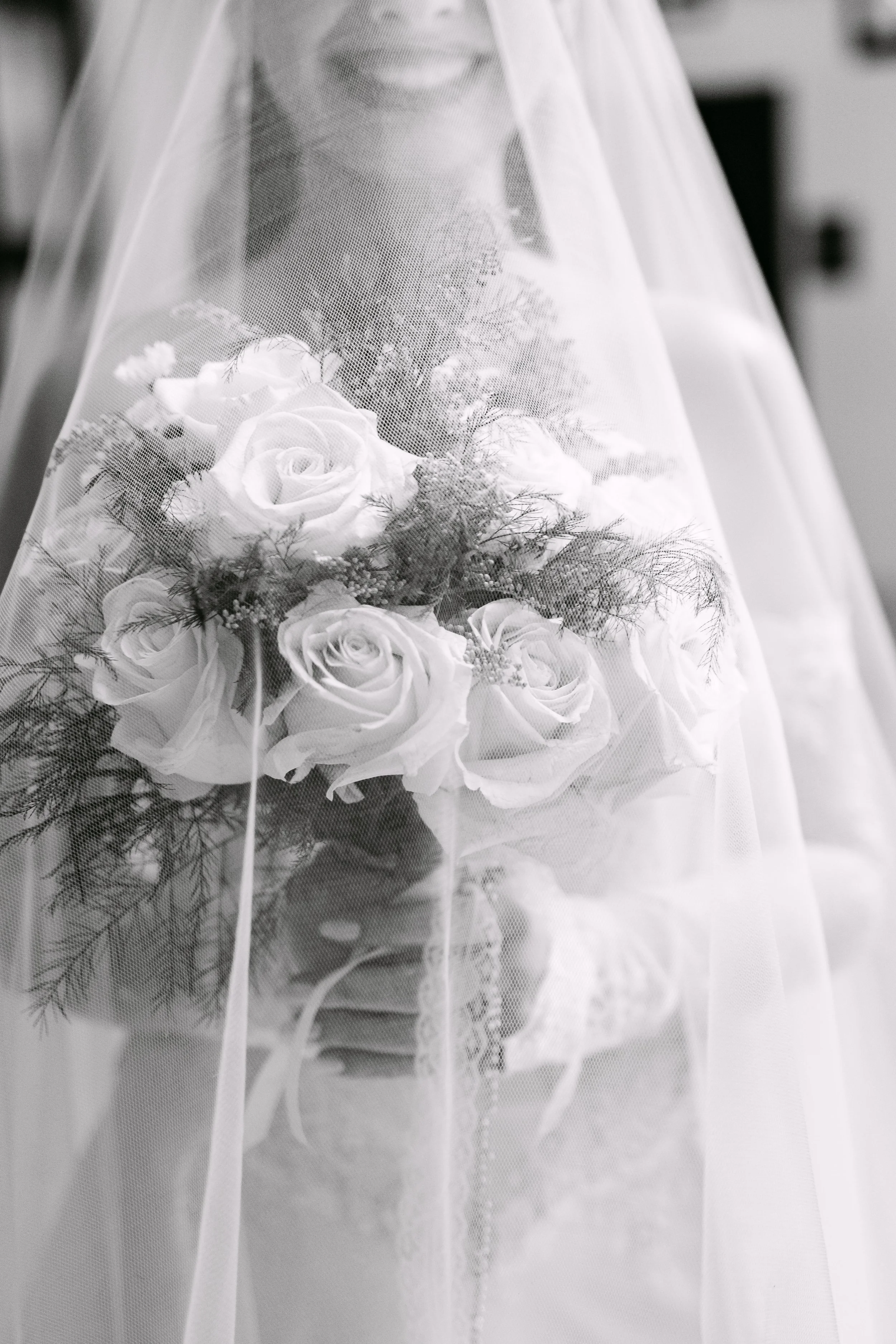 Novia con velo cubriendo su rostro, sosteniendo un ramo de rosas blancas, en una fotografía en blanco y negro.