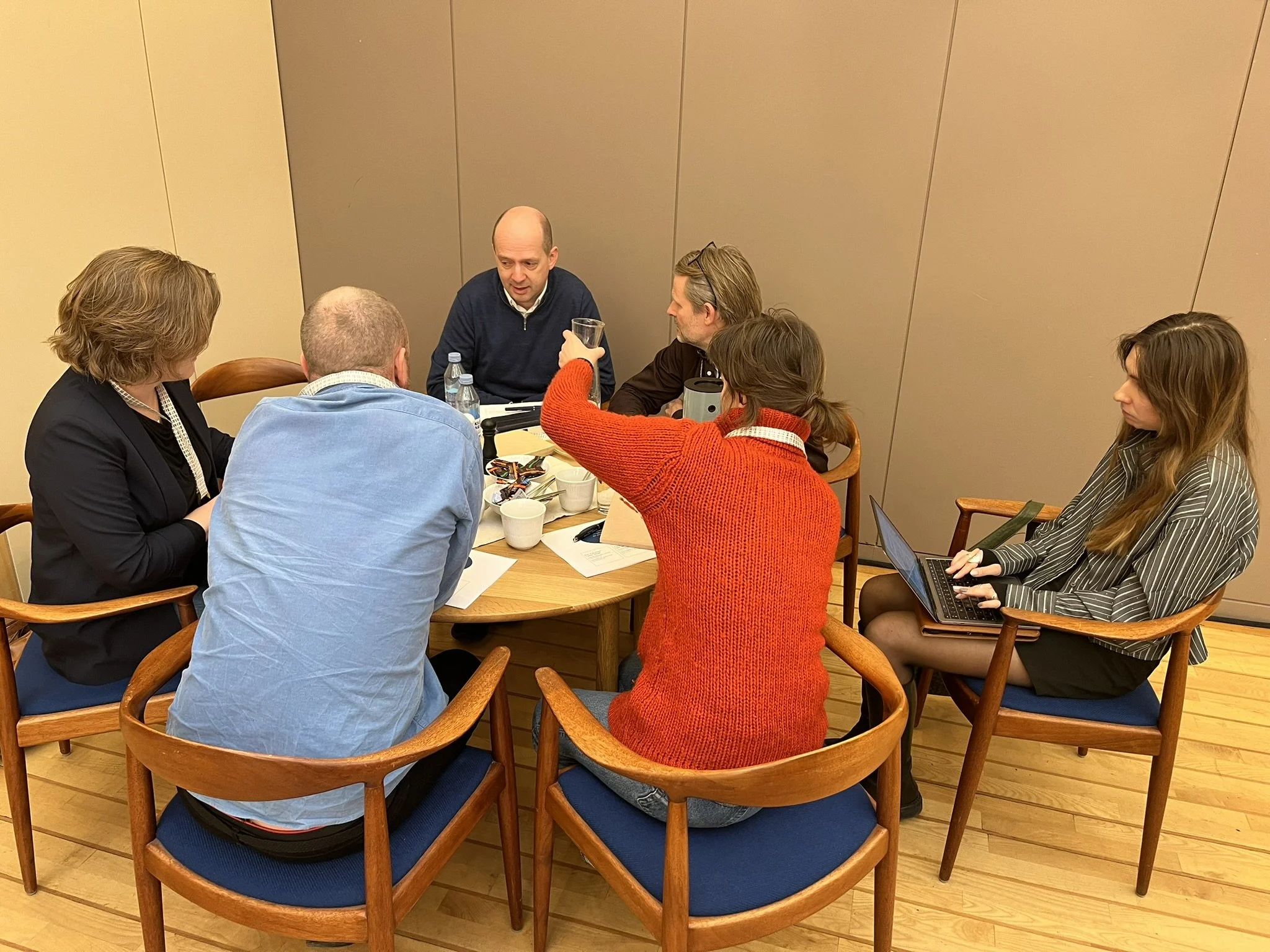 Rundbordssamtaler ved Symposium i Forum for En Ny Grøn Oplysningstid. Gruppe mennesker sidder rundt et ovalt bord, taler og arbejder sammen i et mødelokale.
