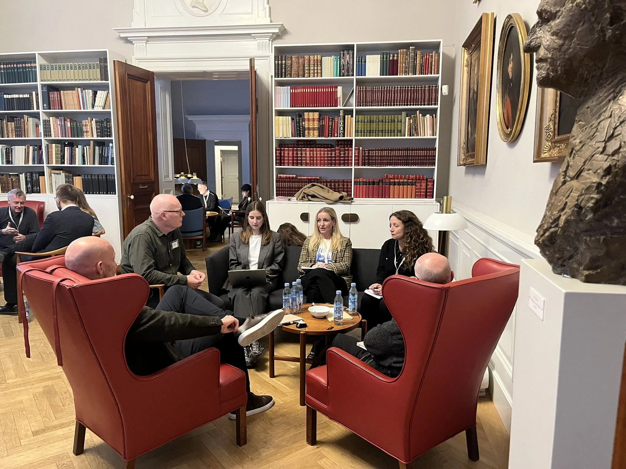 Rundbordssamtaler ved Symposium i Forum for En Ny Grøn Oplysningstid. Folk sidder og taler i en bibliotekslignende stue med store bogreoler på væggene.