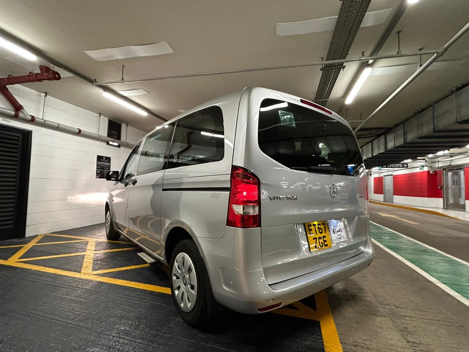 Silver Mercedes-Benz Vito van parked in an underground parking garage near a wall with fire sprinkler system and a green parking space marking.