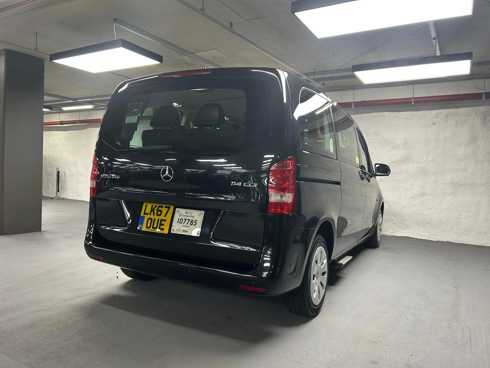 Black Mercedes-Benz Vito van parked in an indoor parking garage with overhead fluorescent lights.