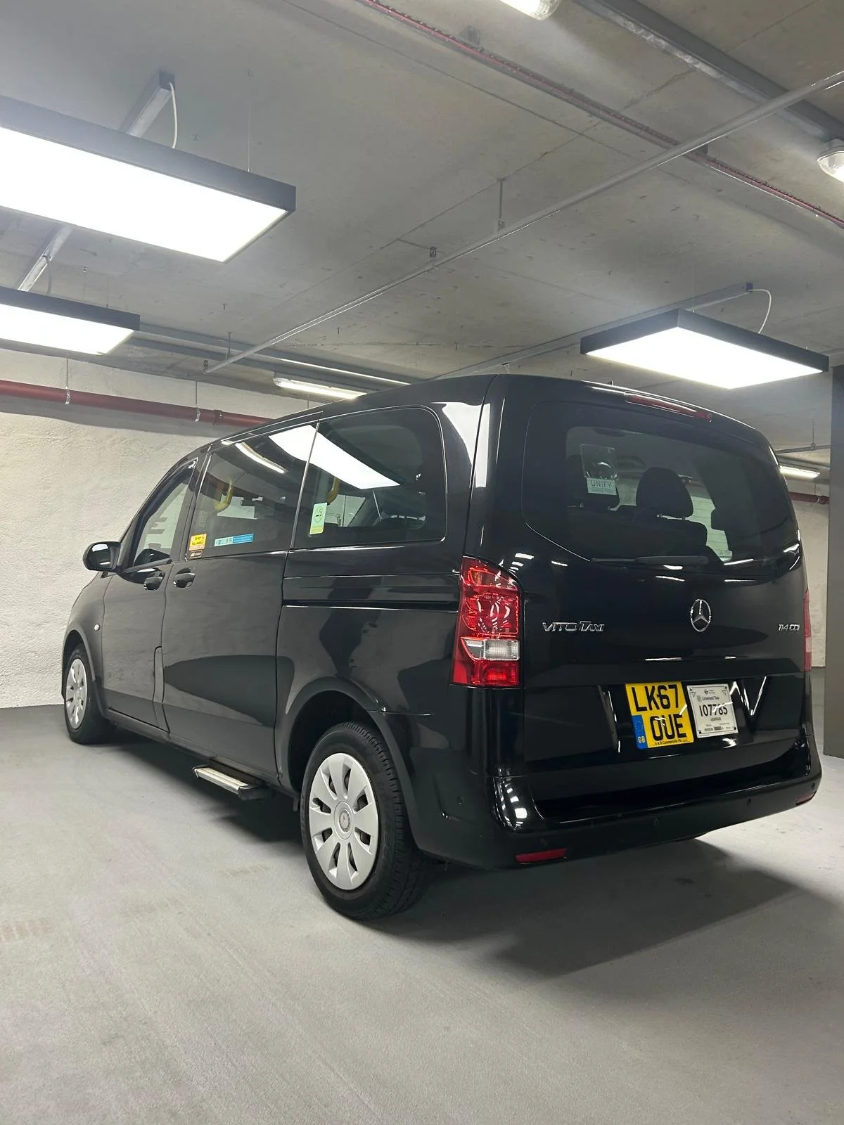 Black Mercedes-Benz Vito van parked in an indoor parking garage with fluorescent ceiling lights.
